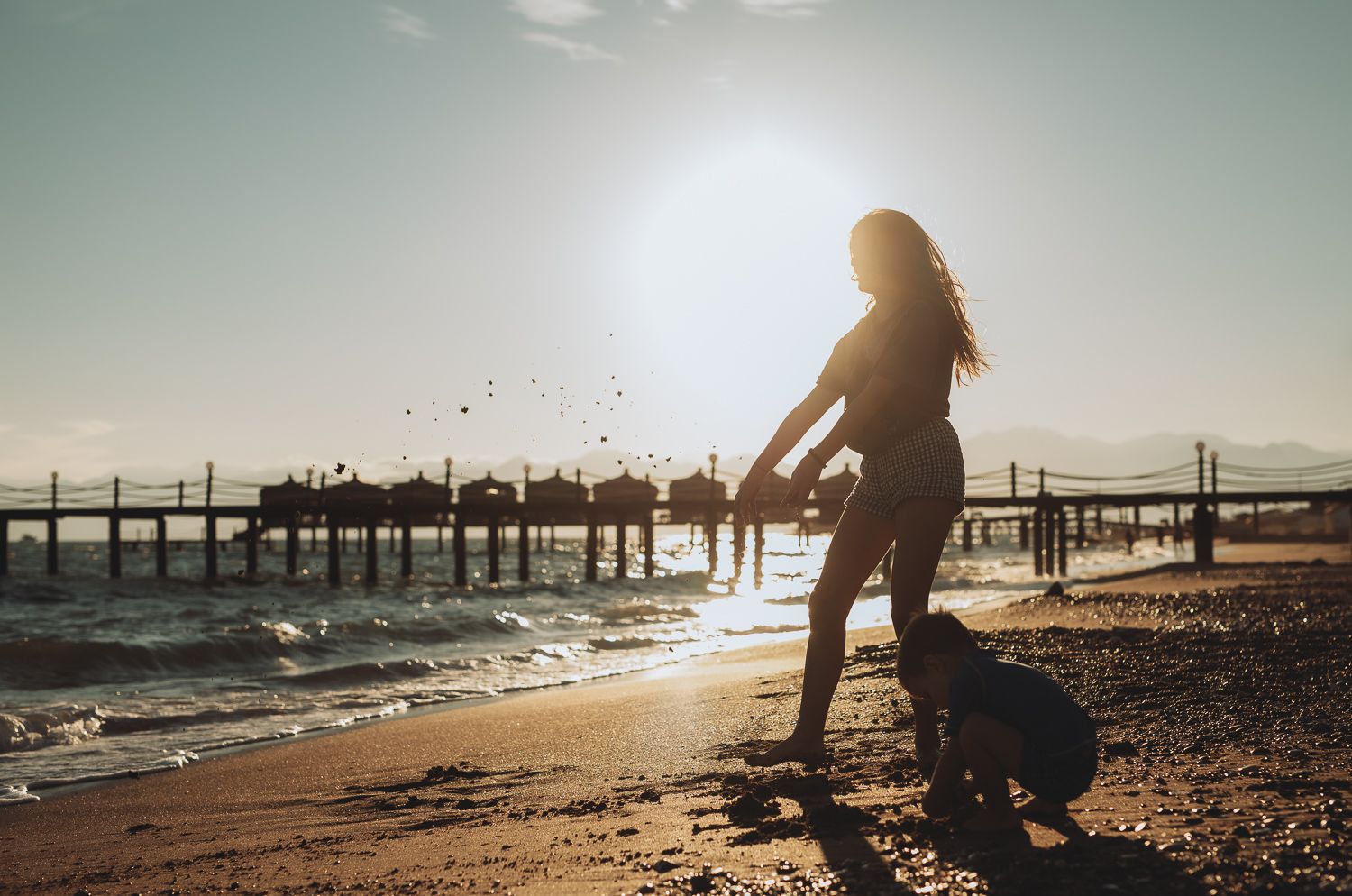 Children playing on a sunny beach near a pier, natural family portrait.