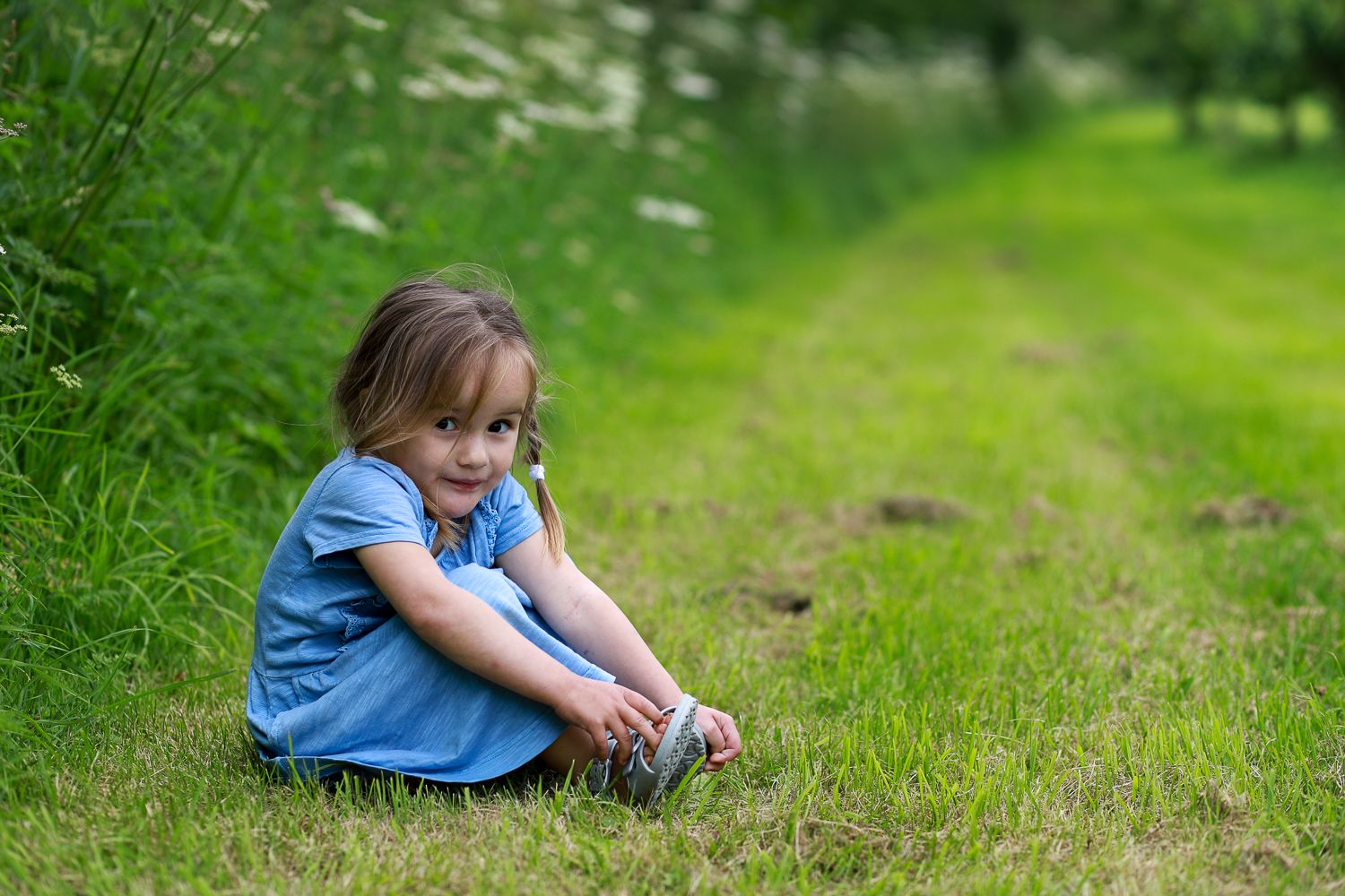 A girl sitting  on the ground smiling during natural family photography session in summer