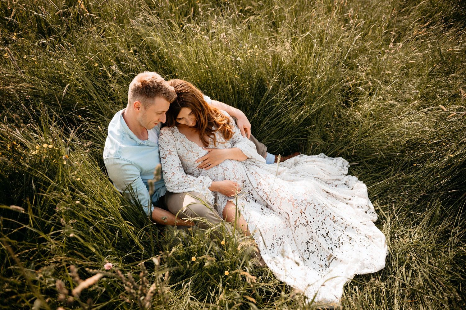 Paar mit Babybauch im Feld bei Sonnenlicht – natürliche Babybauchfotografie in Nürnberg