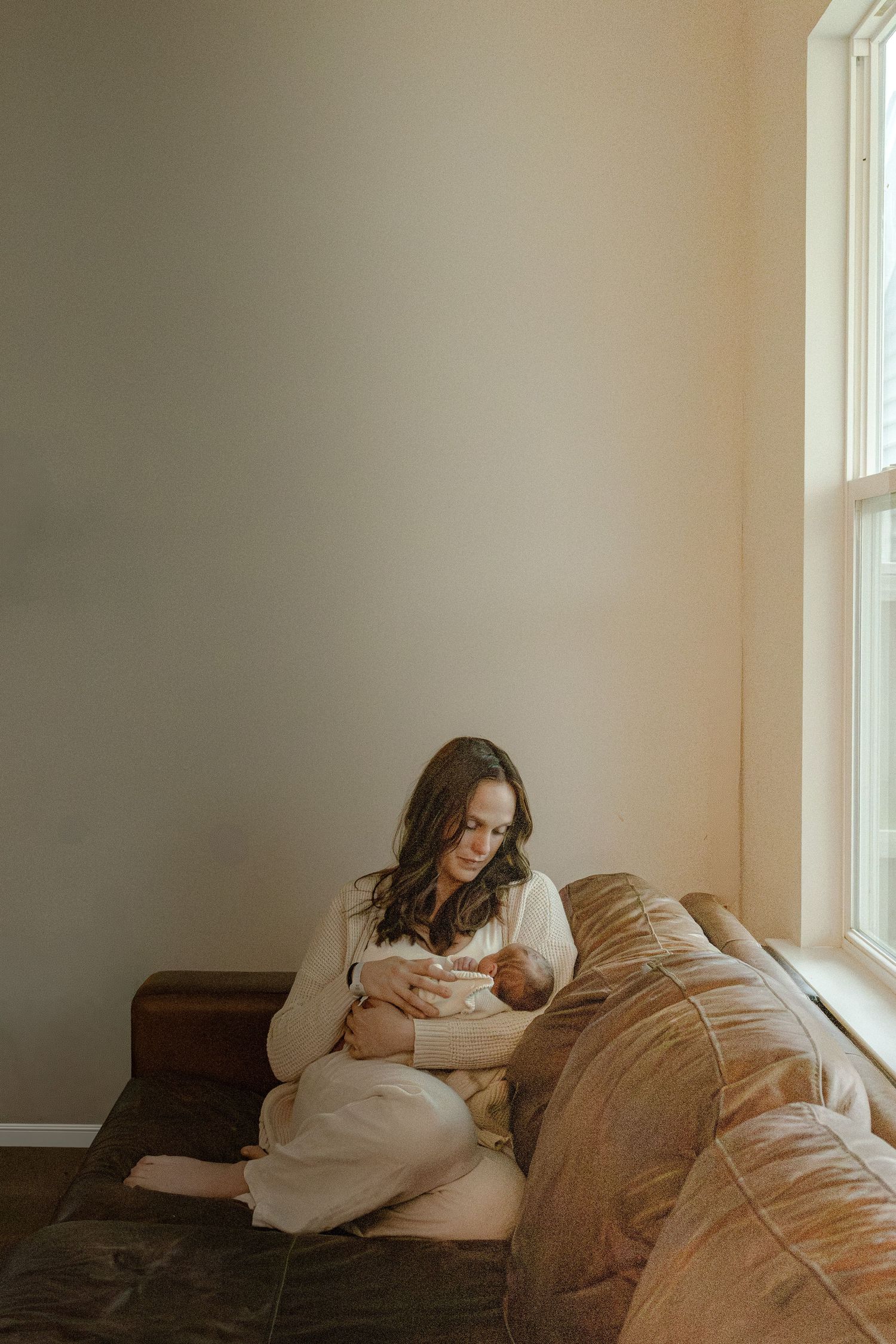 A person relaxes on a beige couch near a window in a minimalist room with natural lighting.