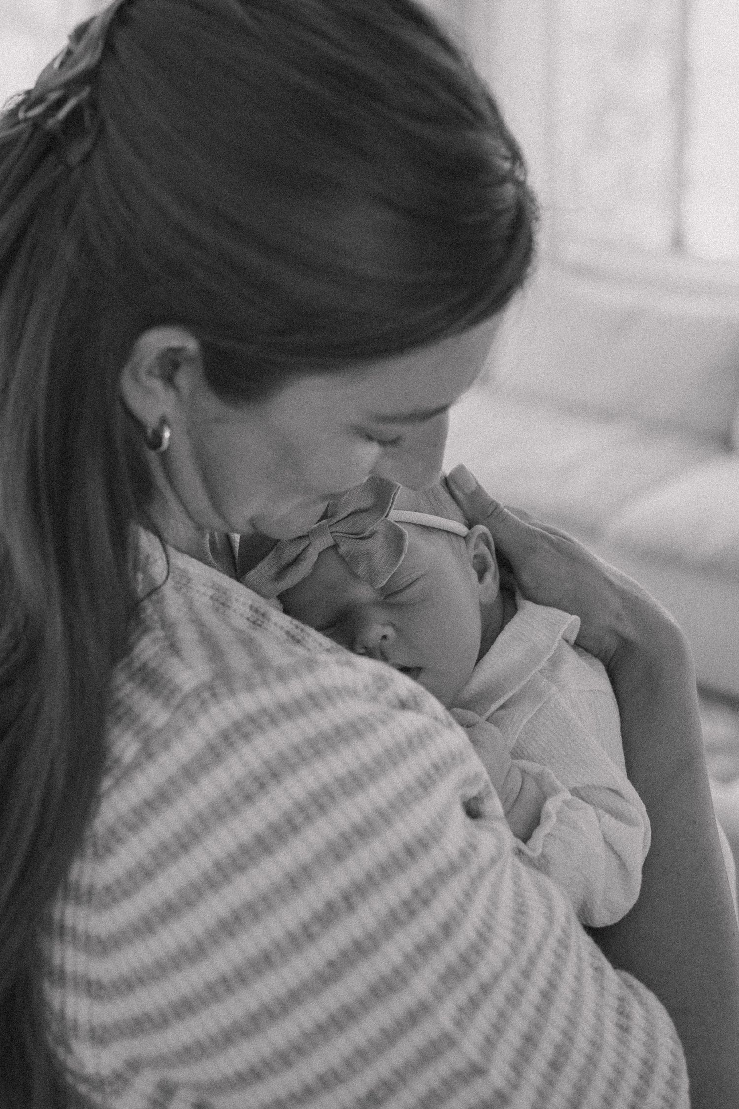 Black and white photo of a mother tenderly kissing her newborn baby while cradling it in her arms.