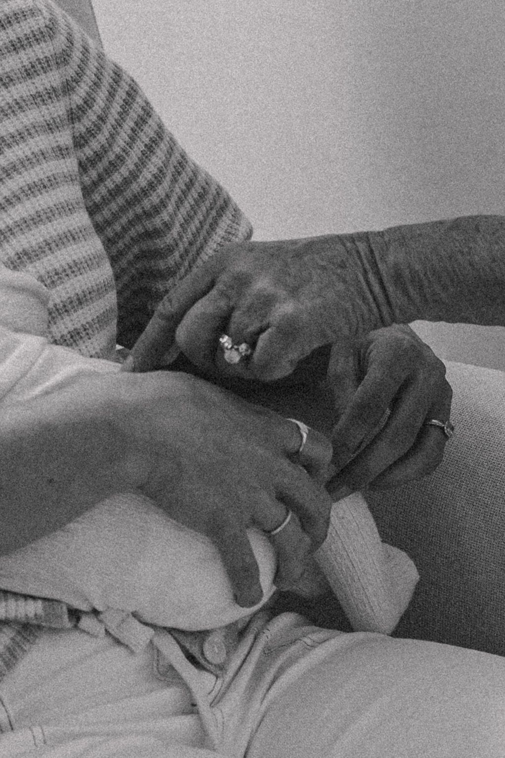 Black and white photo of two people holding hands, wearing rings, a tender moment of connection.