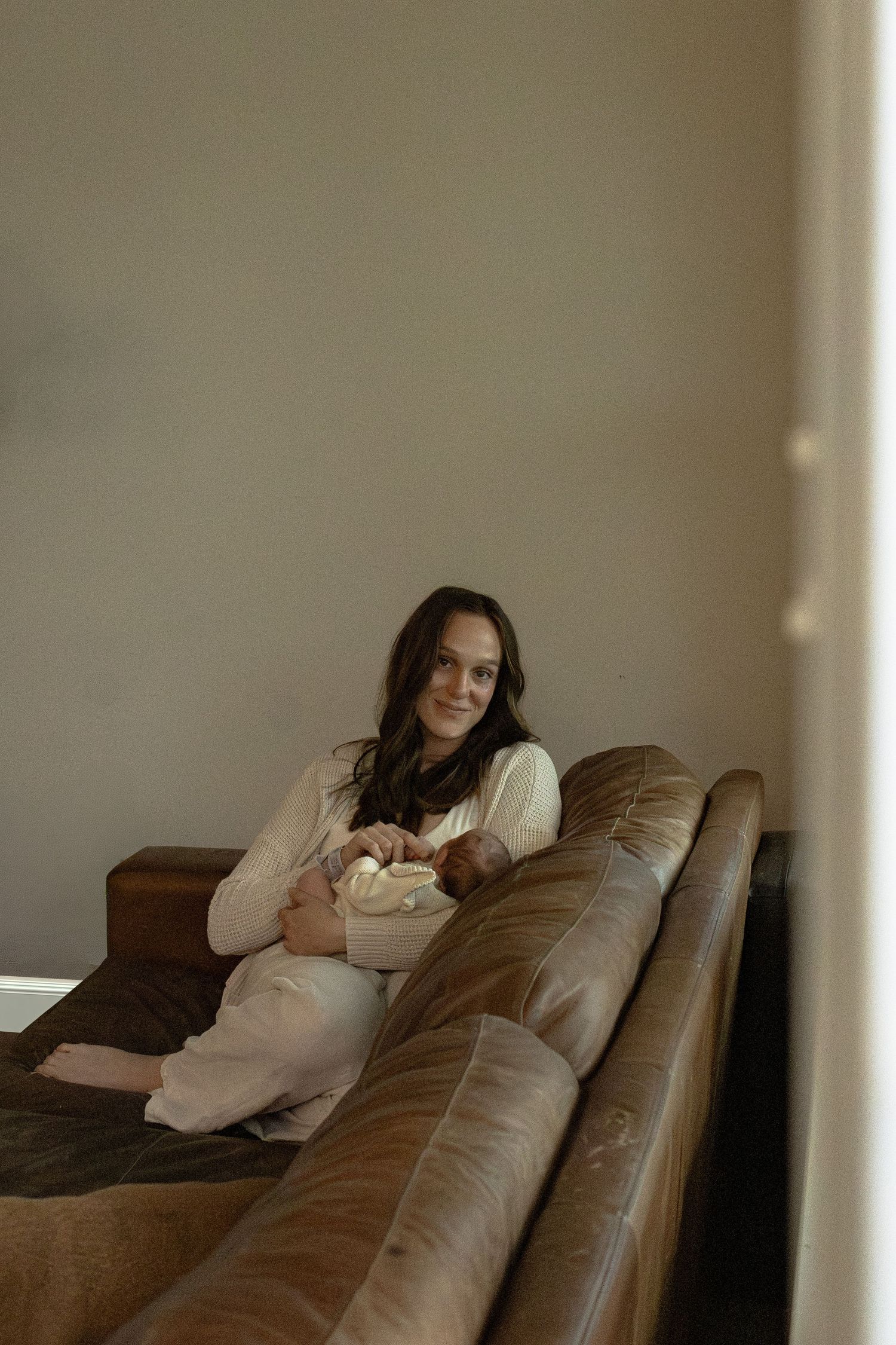 Someone relaxes on a brown leather couch in a cozy living room while holding a bowl.
