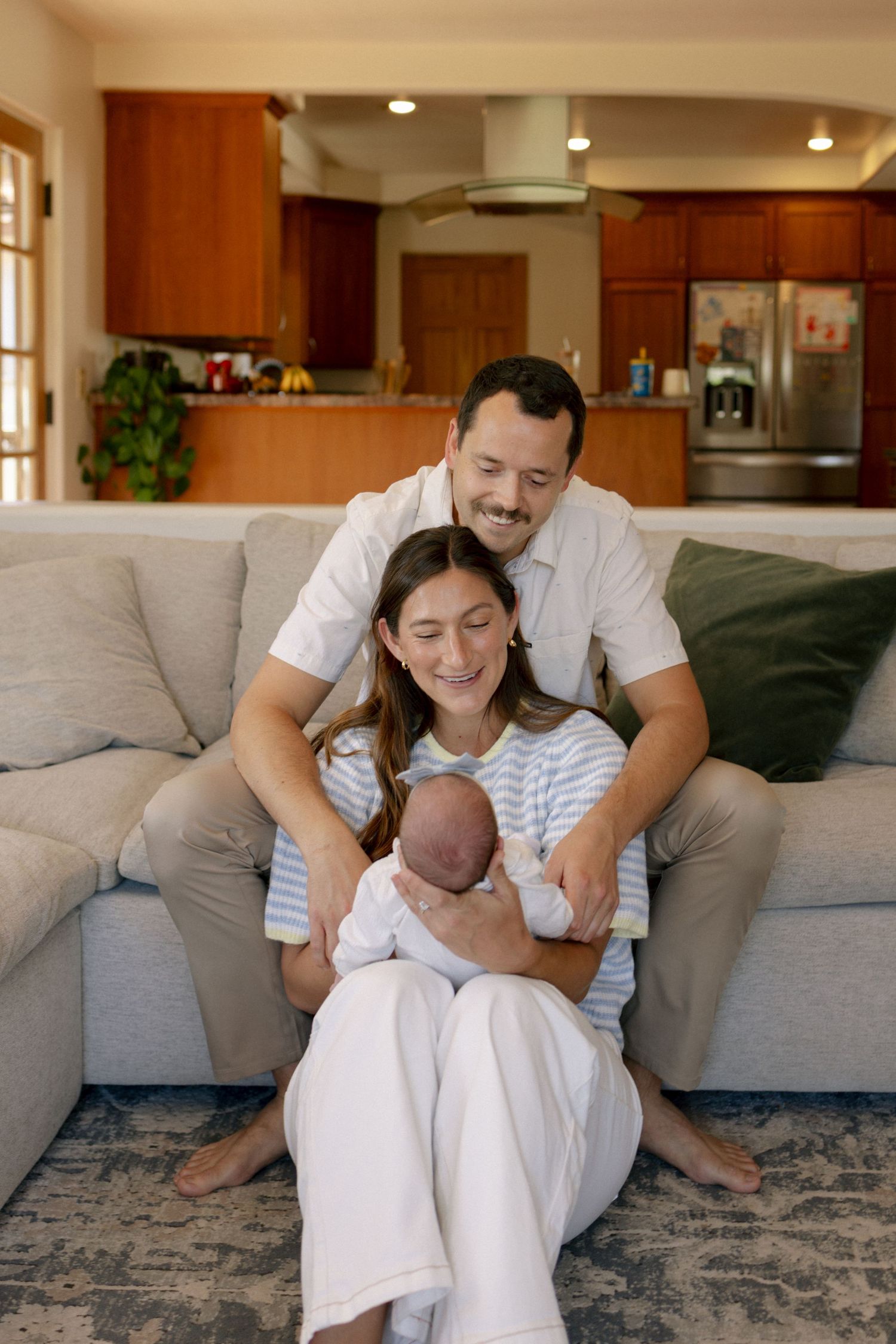 Happy couple sitting on couch at home smiling at their newborn baby in a cozy living room.