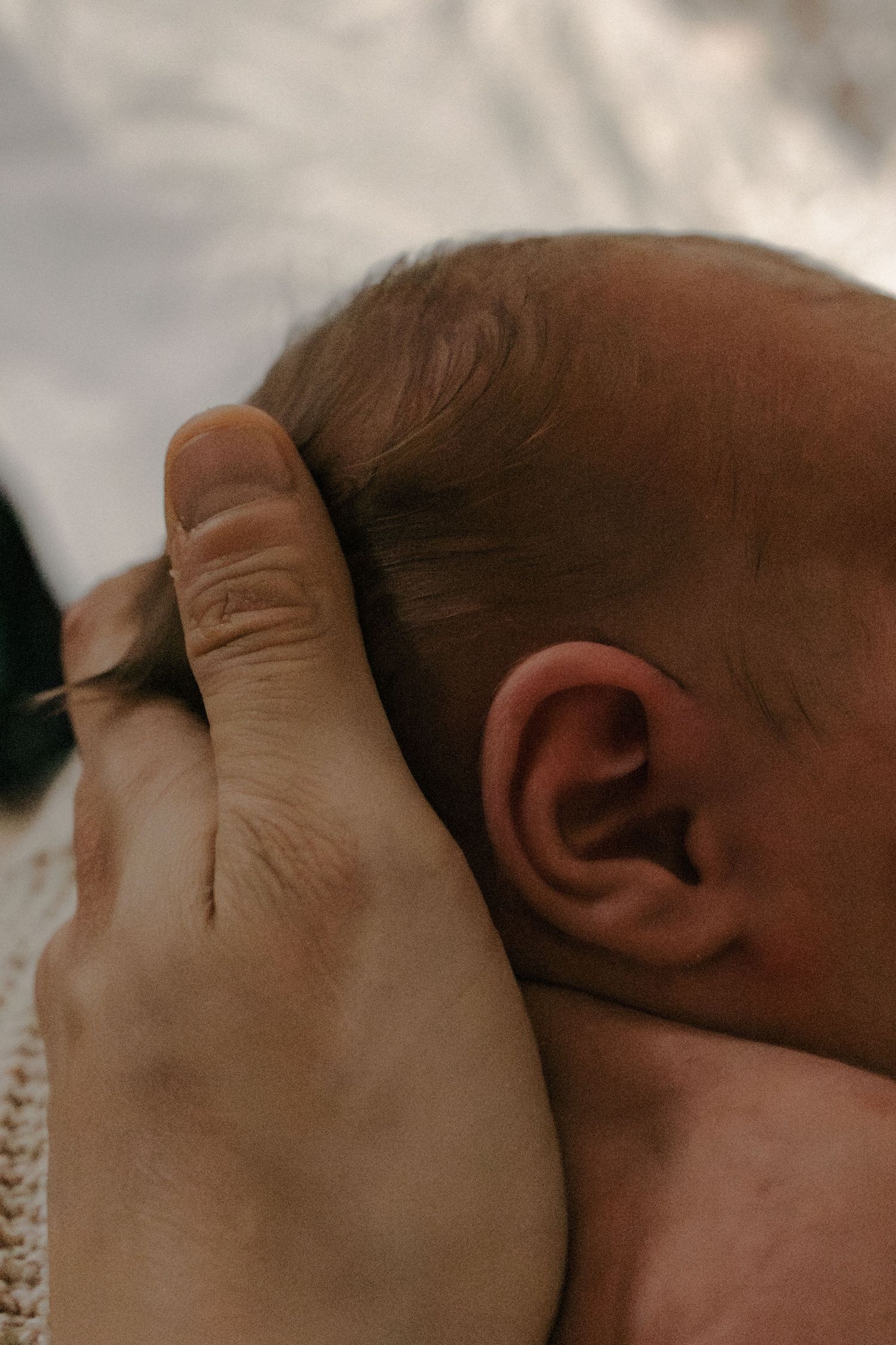A close-up profile view of a baby's head and ear against a soft neutral background.