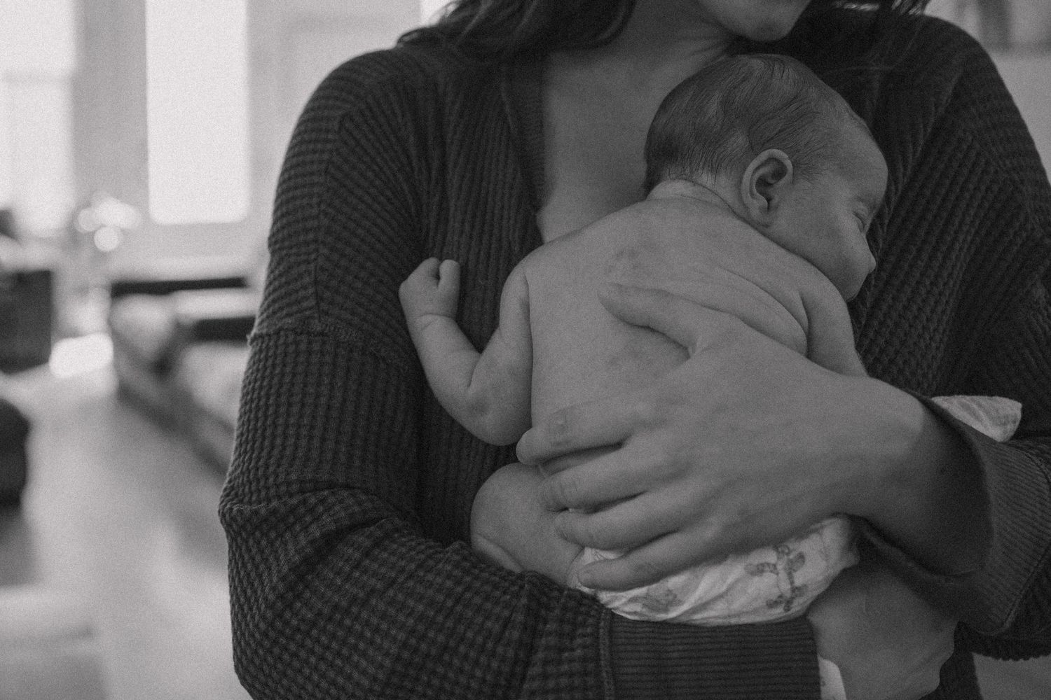 A black and white image of a sleeping newborn baby being cradled in someone's arms wearing a knit sweater.