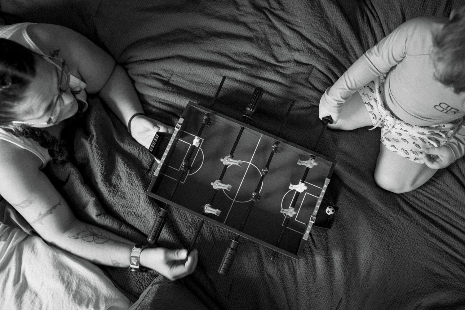 Black and white image of video game controllers on dark bedding.
