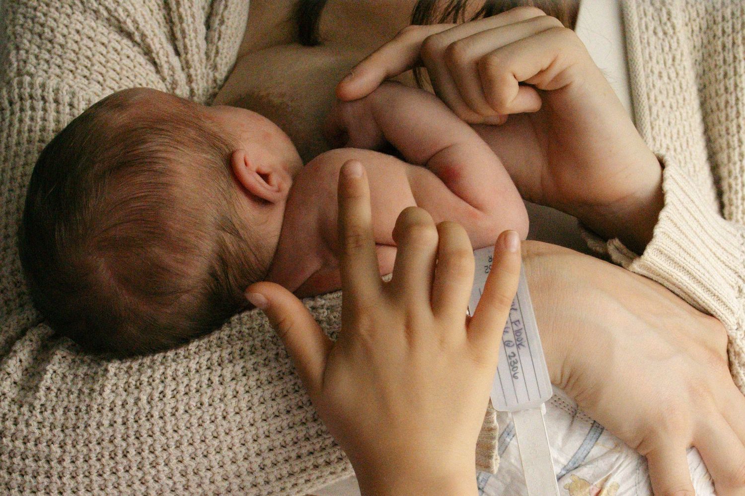 A small baby rests peacefully in a cozy knit blanket while being gently held.