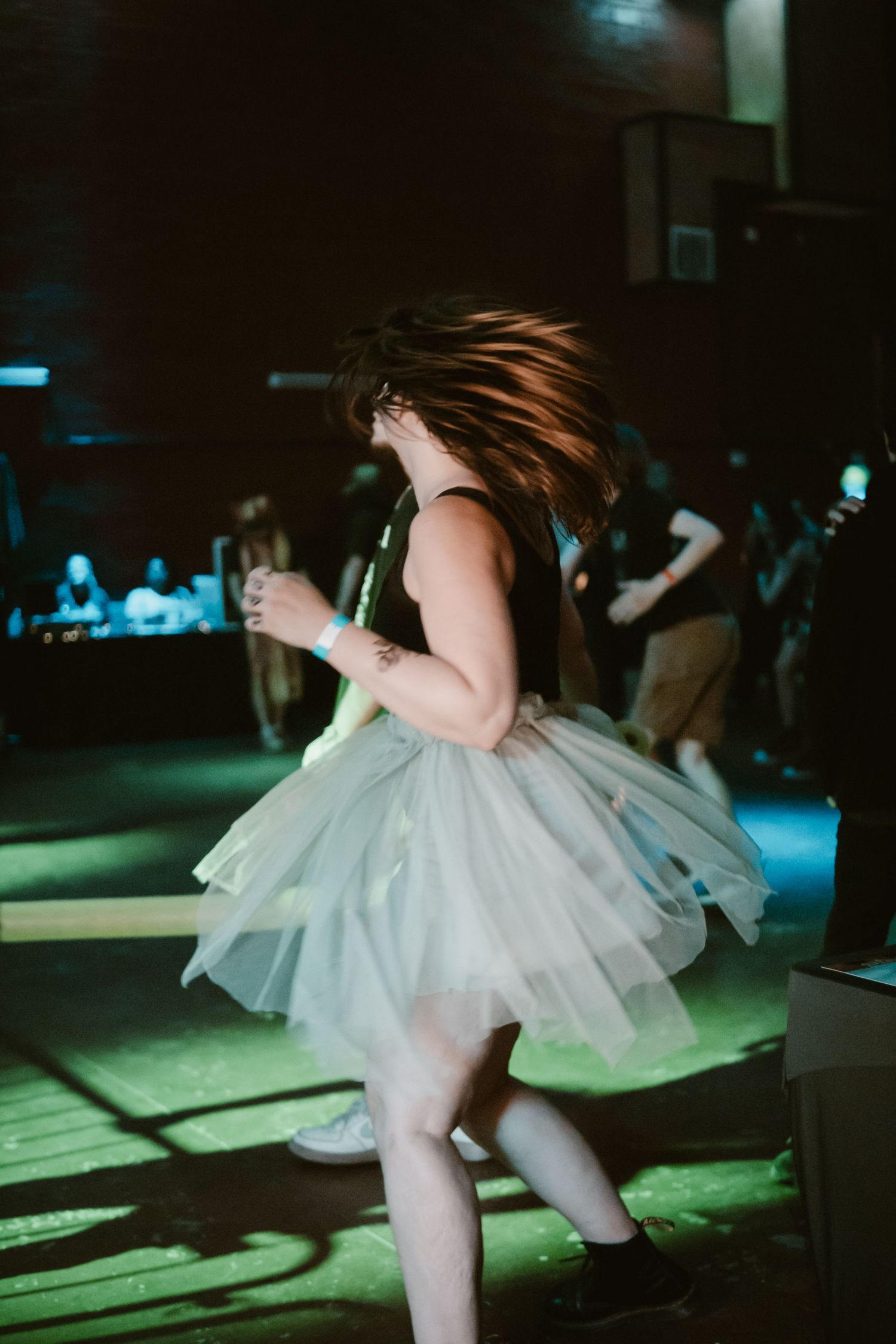 Woman in white tutu dress headbanging energetically on stage under green concert lighting.