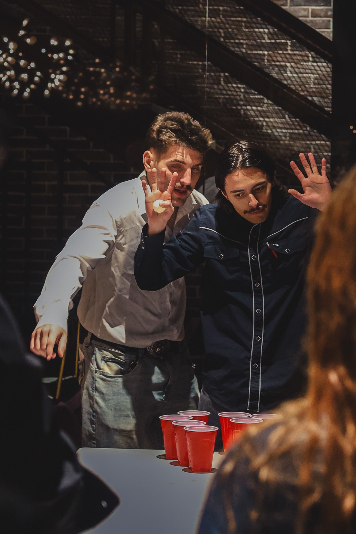 Two men playing beer pong, raising hands in excitement at an indoor party with red Solo cups on table.