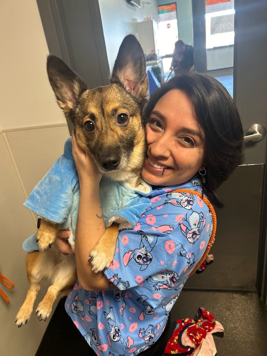 Smiling woman holding a German Shepherd puppy wearing a light blue shirt indoors.