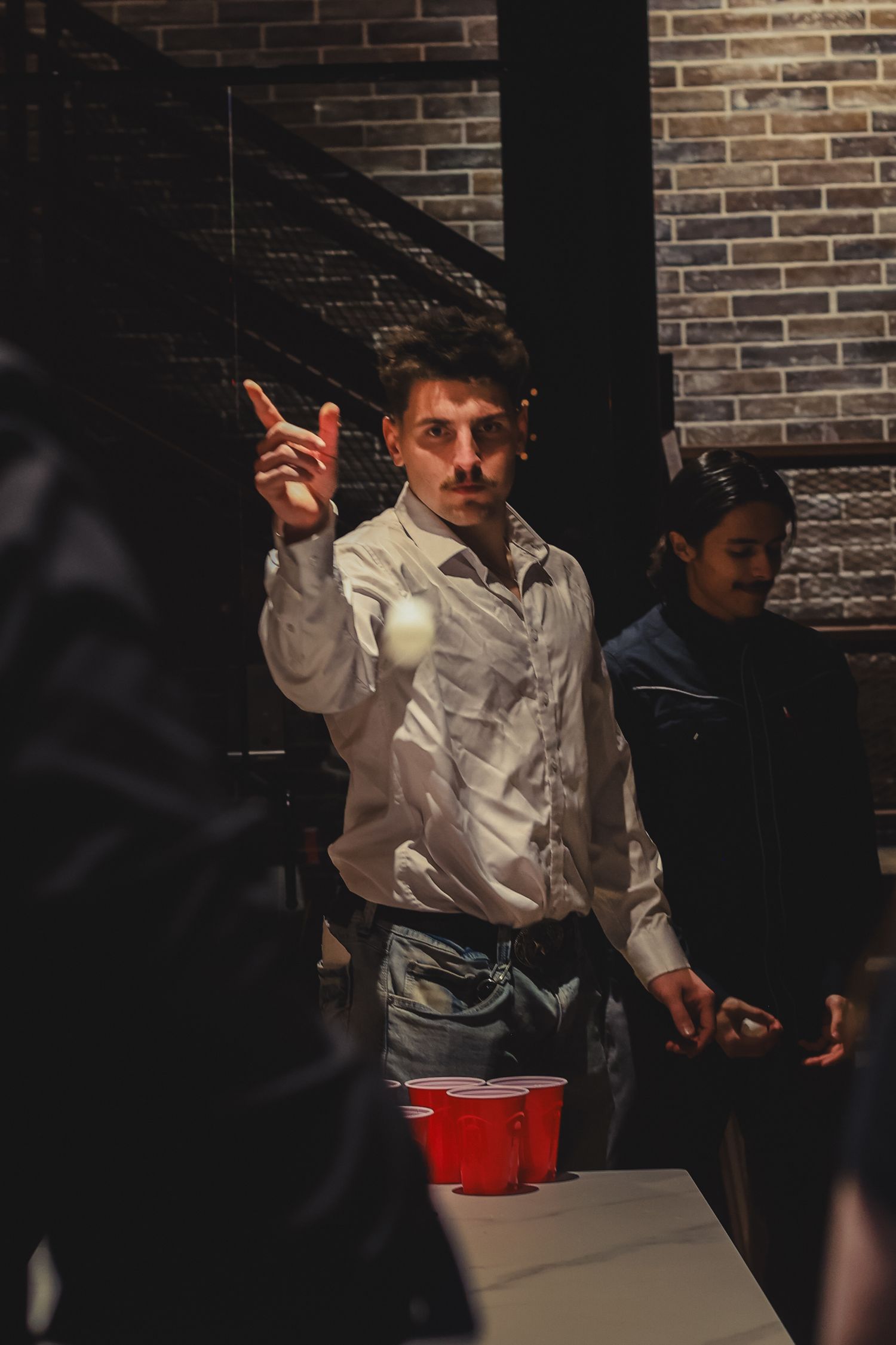 Young man in white shirt playing beer pong with red cups at a party, tossing a ping pong ball.
