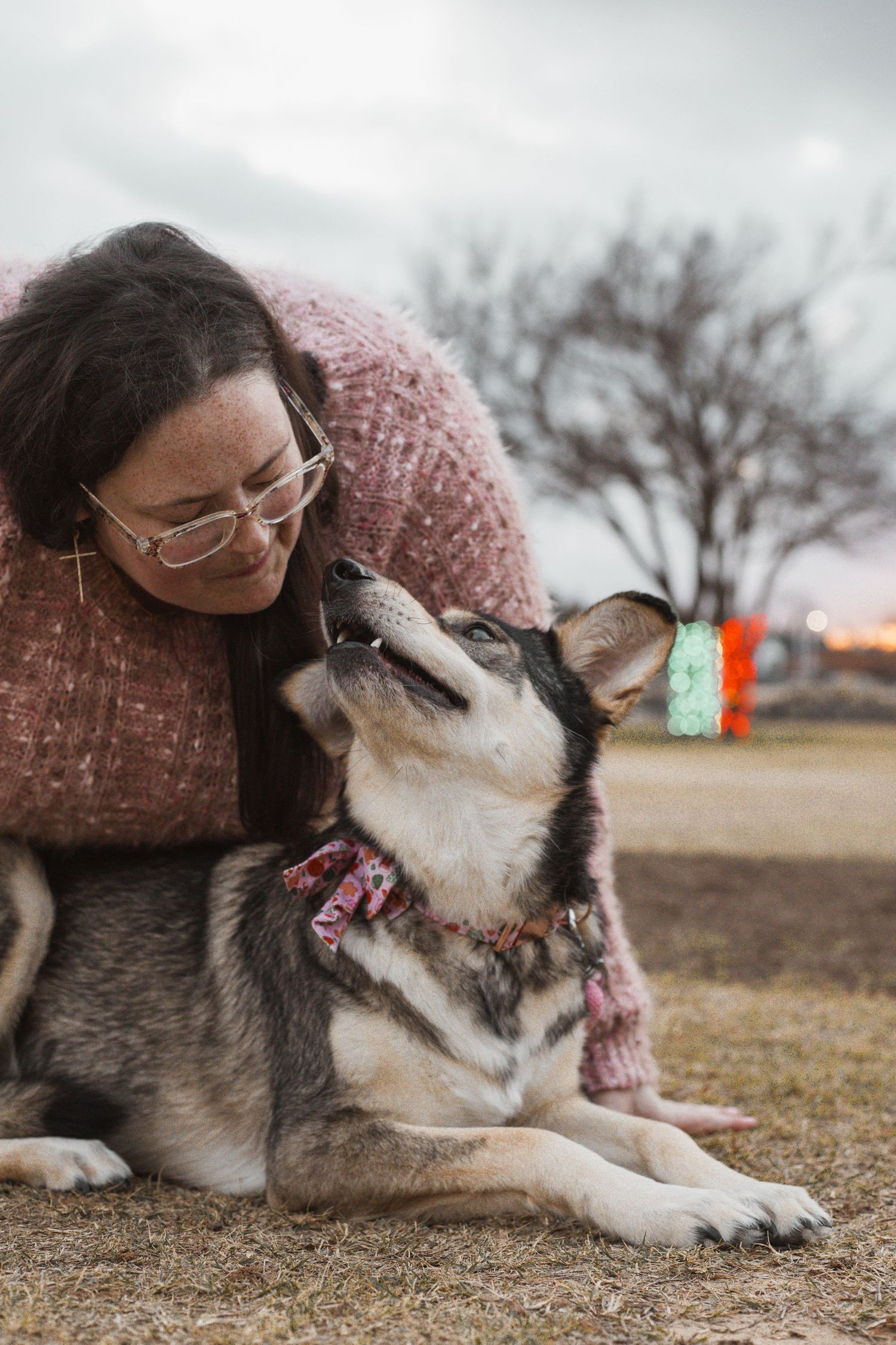 Woman in pink sweater sharing a tender moment with her Husky dog outdoors at dusk.