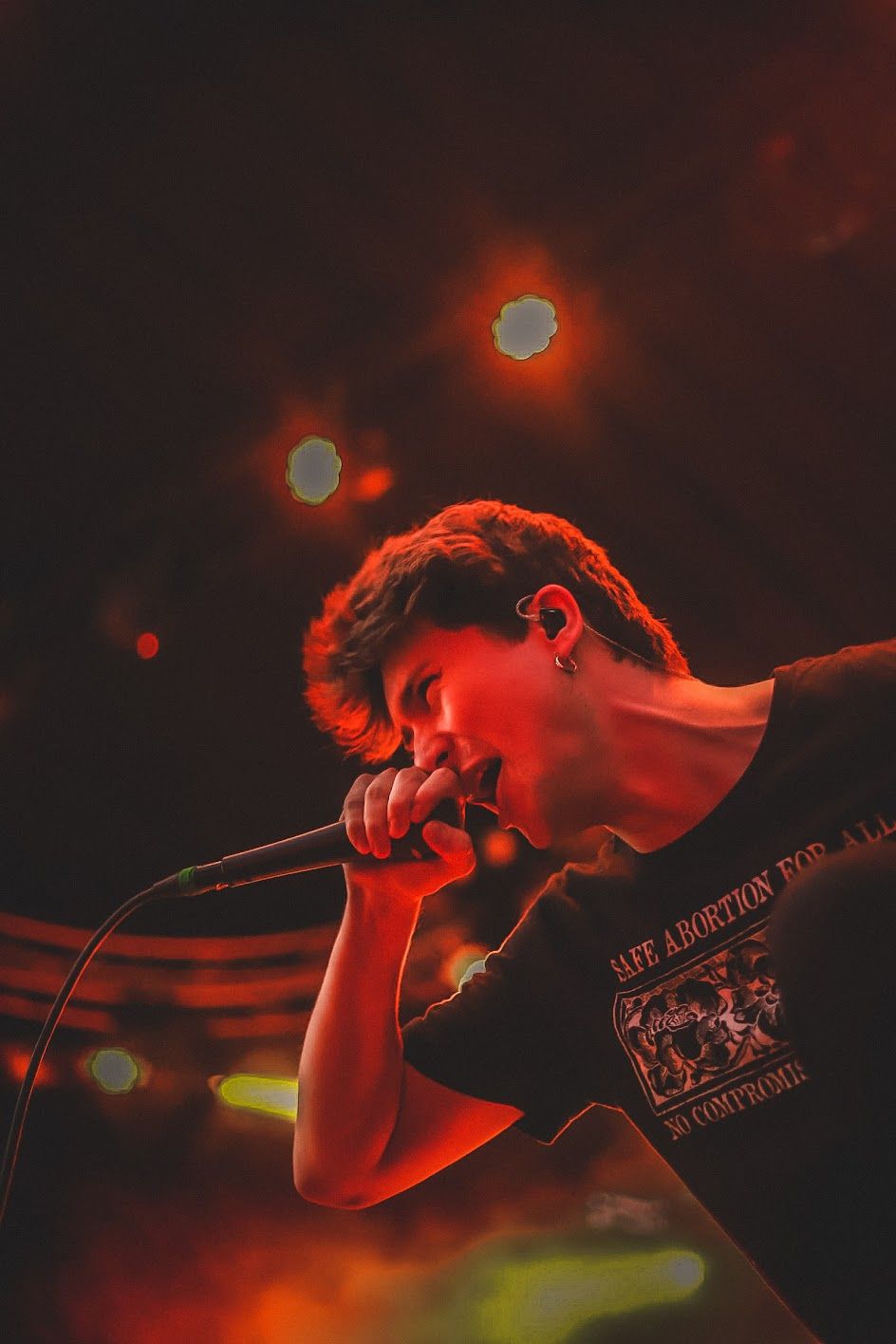 Close-up of a young vocalist singing passionately into a microphone under red concert lighting on stage.
