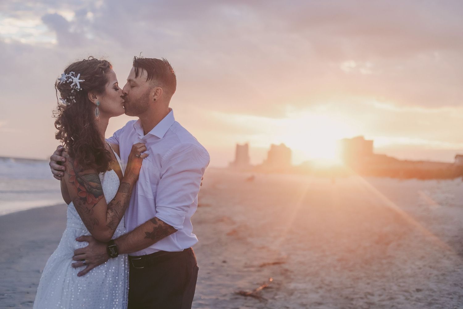 A couple kisses on a sandy beach during a beautiful golden sunset ceremony.
