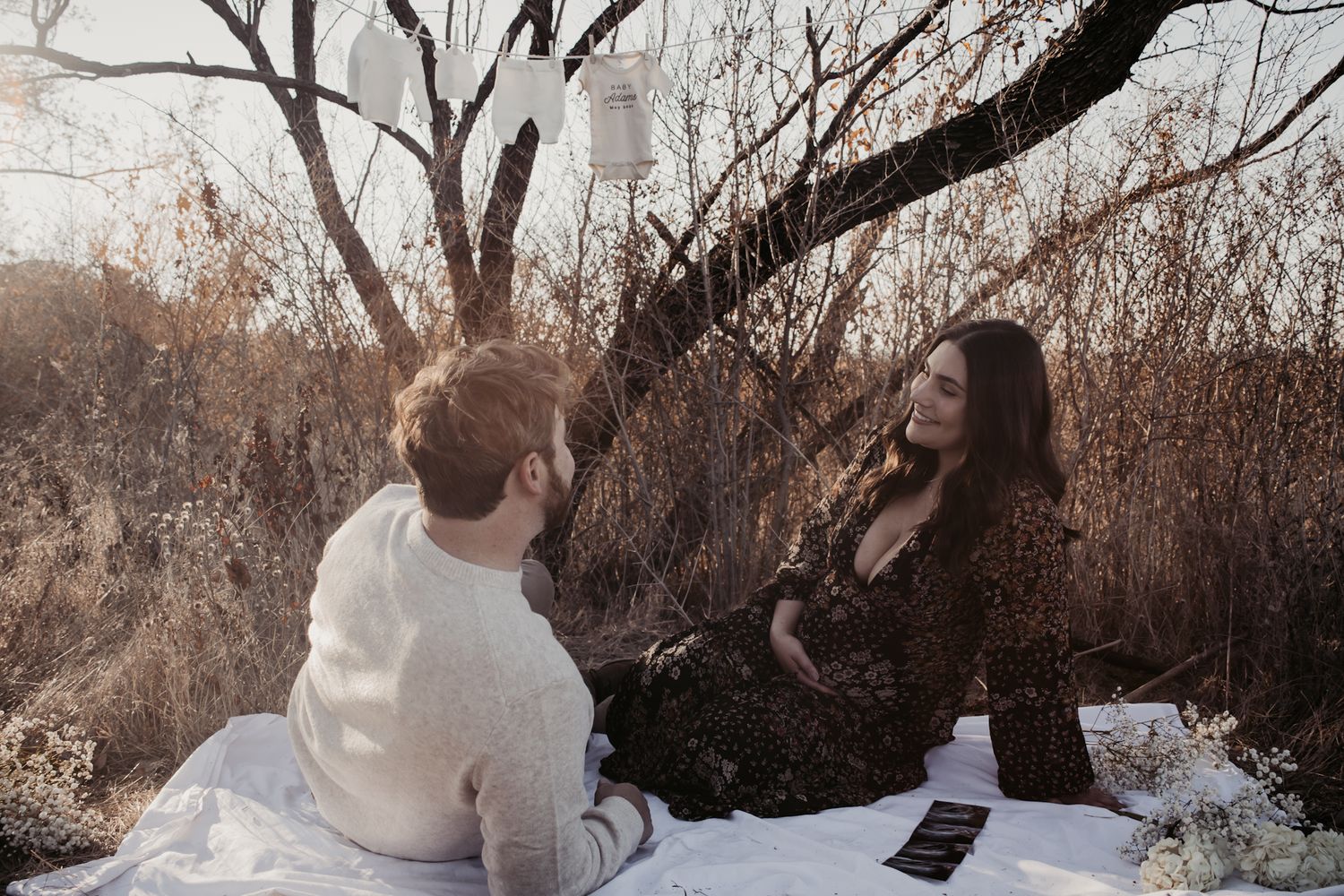 A couple sits together on a white blanket in a sunlit autumn outdoor setting.