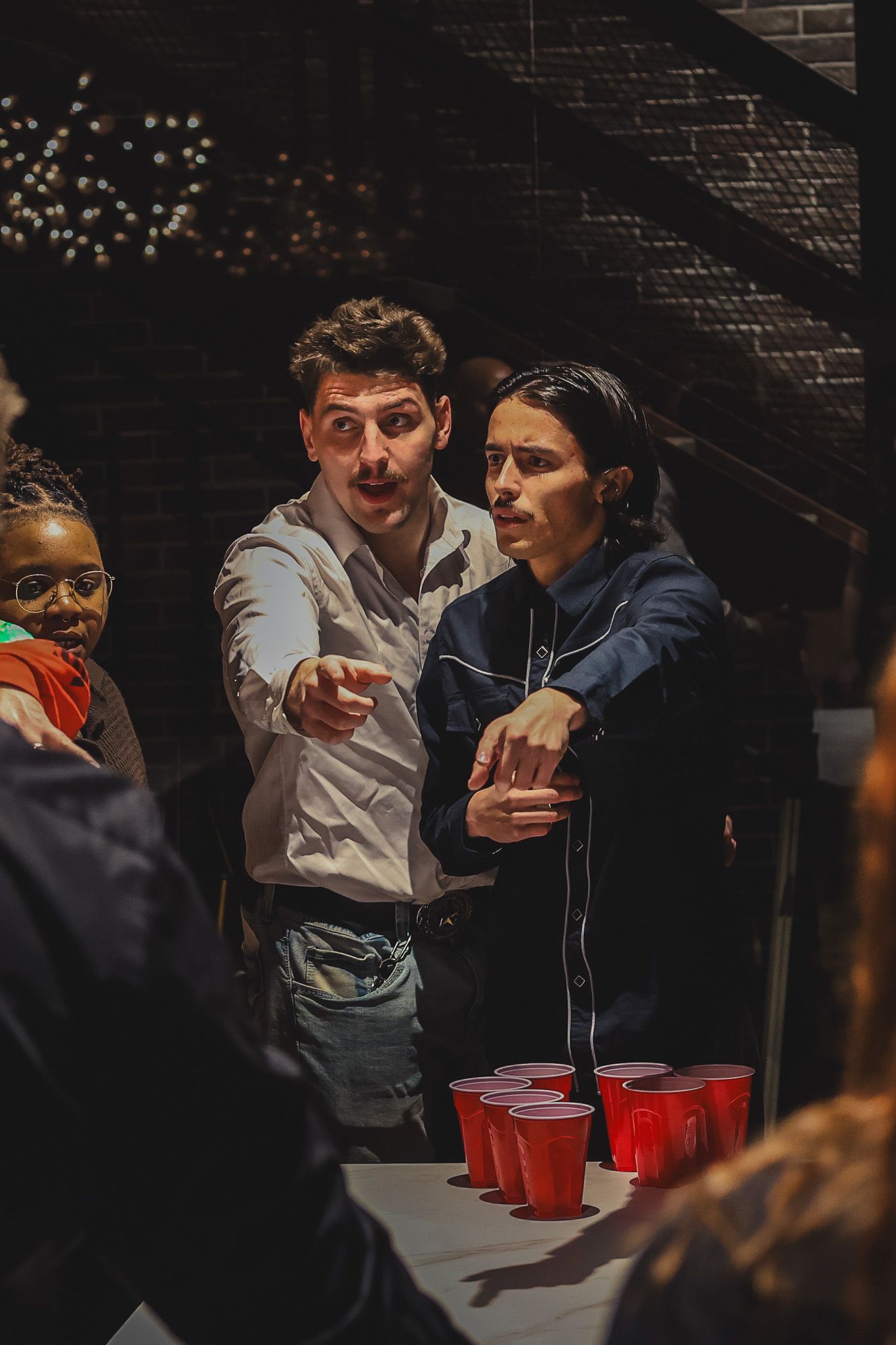 Two people playing beer pong at a party, leaning over a table with red Solo cups.