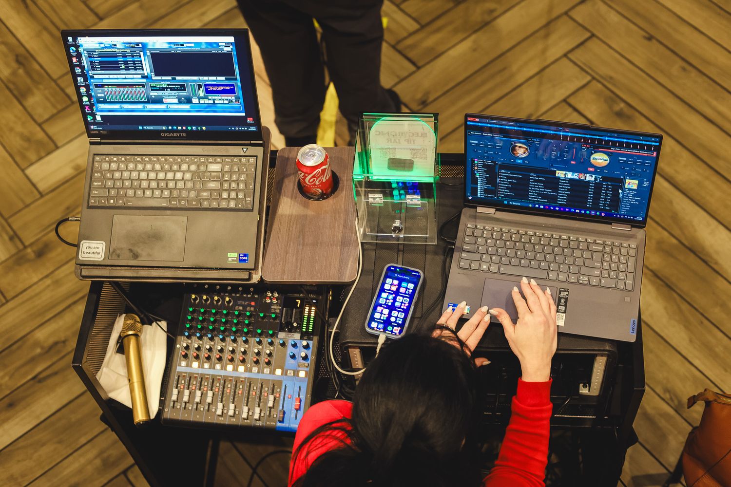 Overhead view of a music producer working on laptops and audio mixer at a wooden desk with a red can drink.