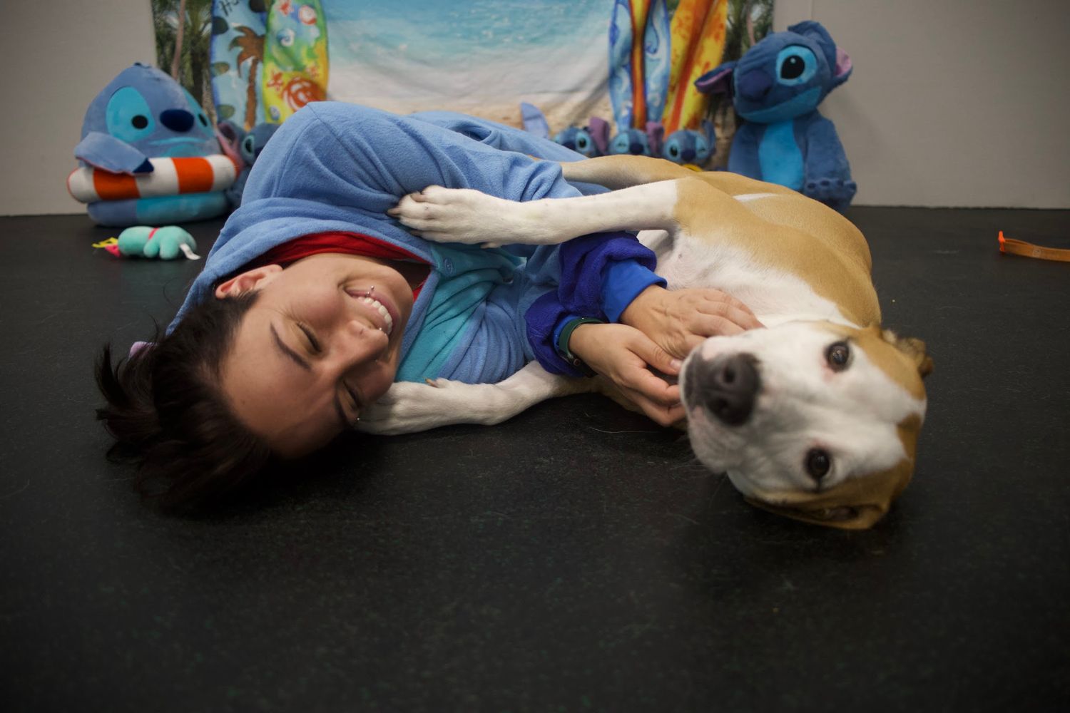 Woman lying on floor laughing while a tan and white dog cuddles beside her.