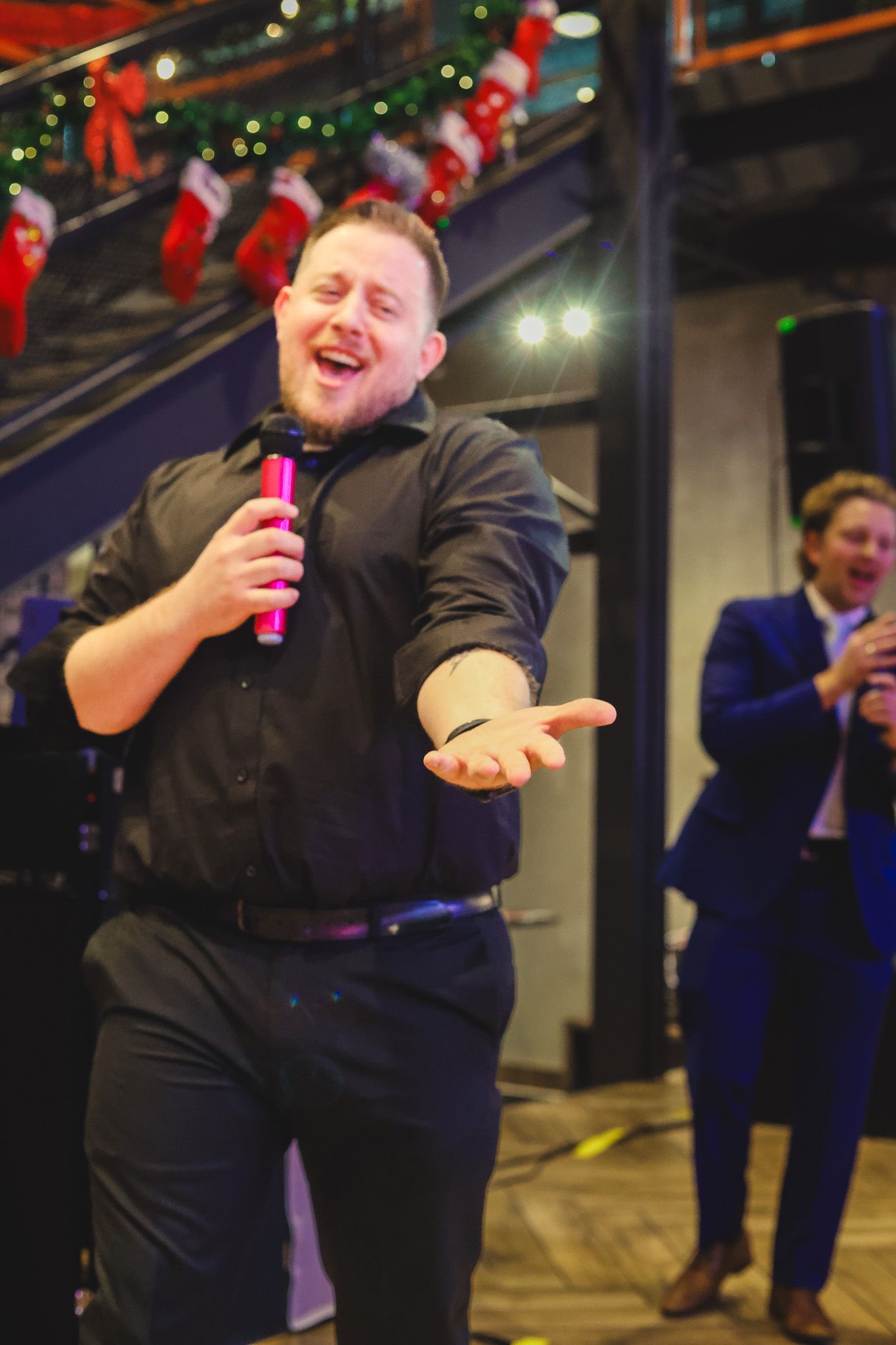 Man passionately performs with pink microphone at a holiday party with festive decorations.