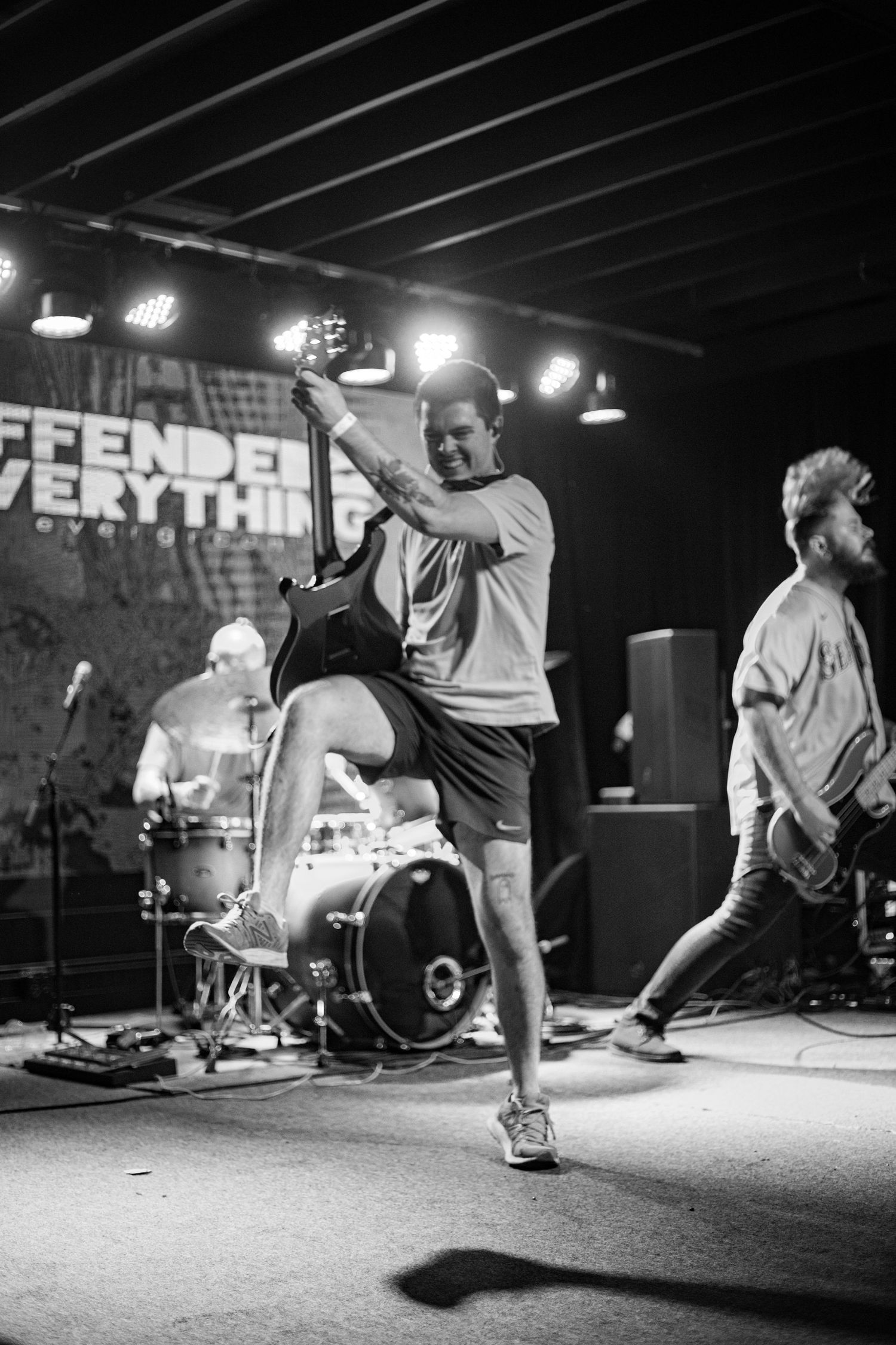Black and white photo of an energetic guitarist kicking his leg on stage during a live show.