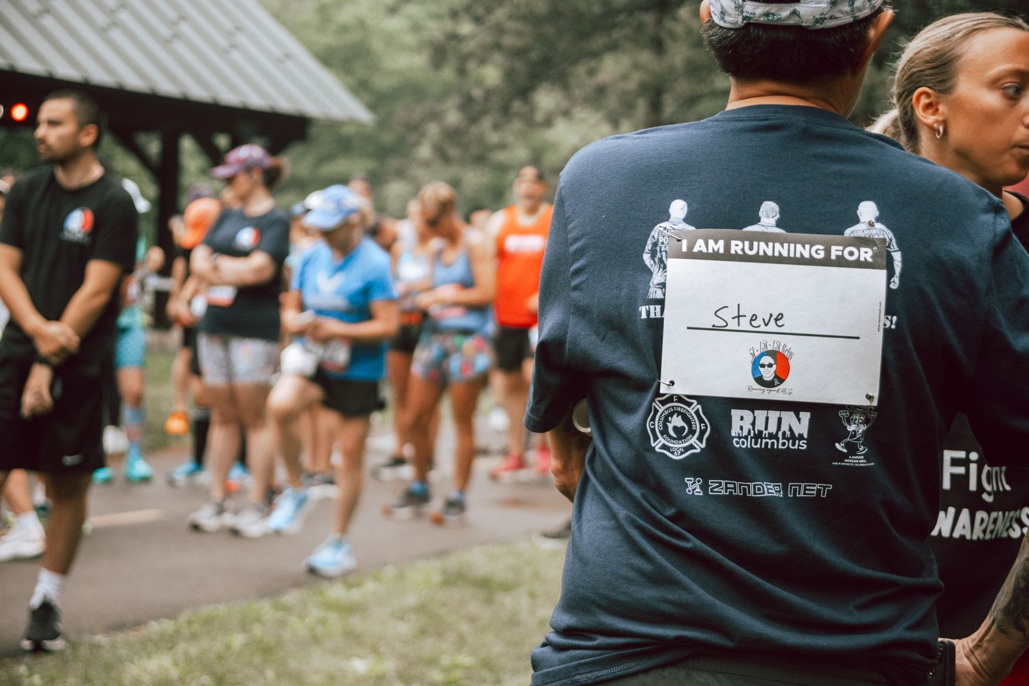 Runner wearing a charity race bib reading Steve at an outdoor fun run event surrounded by other participants.