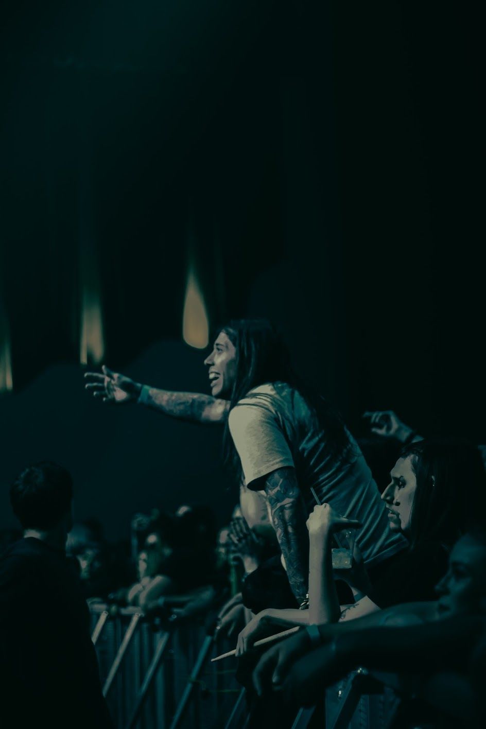 Tattooed female fan sitting on shoulders pointing during a live music concert event.