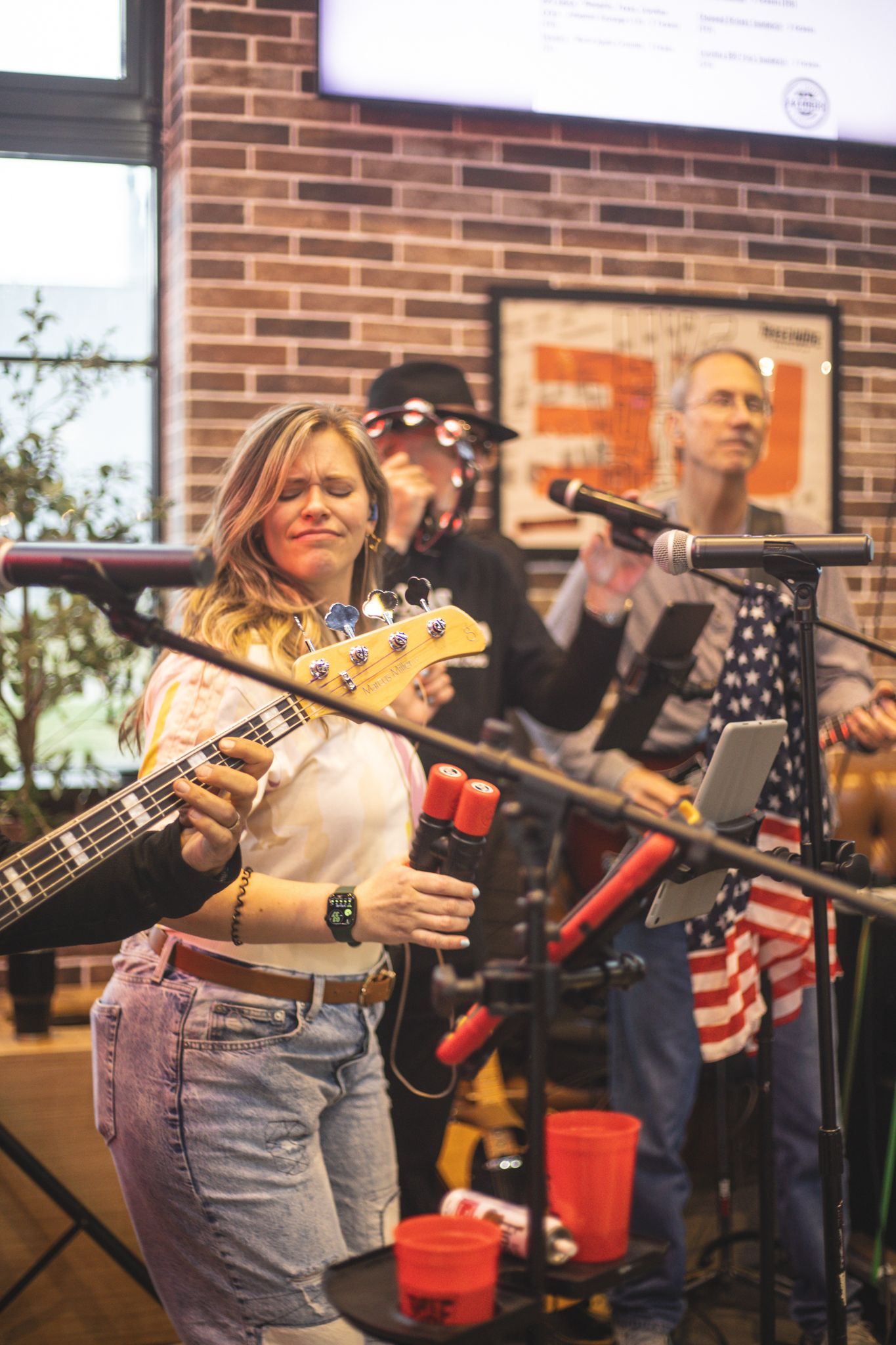 Female bassist playing guitar during a live band performance at an American-themed brewery bar.