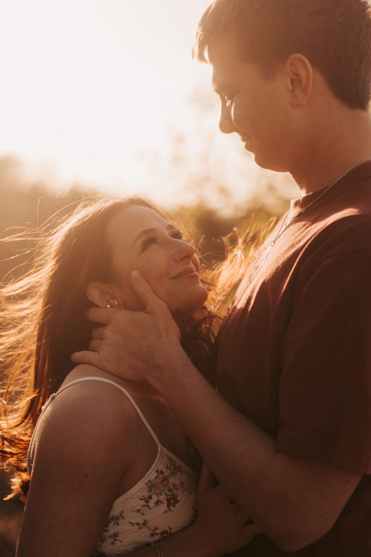 Romantic couple gazing into each others eyes during golden sunset, man tenderly holding womans face outdoors.