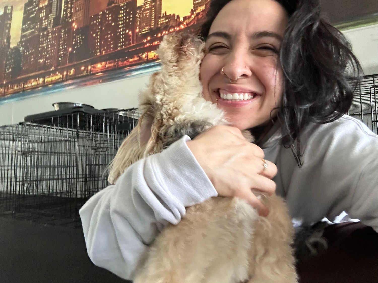 Smiling woman holds and cuddles a fluffy small cream-colored dog in a cozy indoor space.