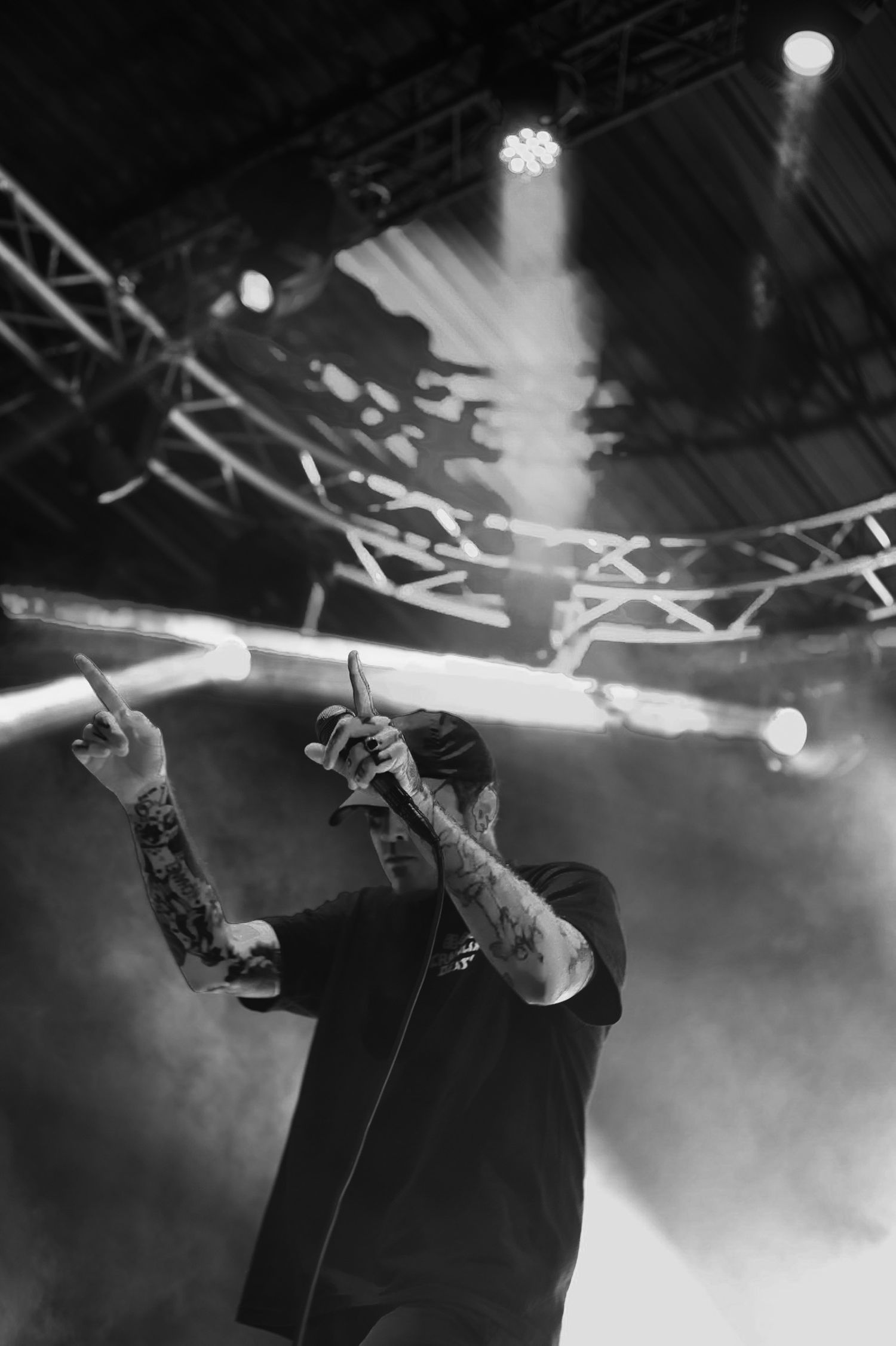 Tattooed performer singing into a microphone under dramatic stage lights and smoke effects.