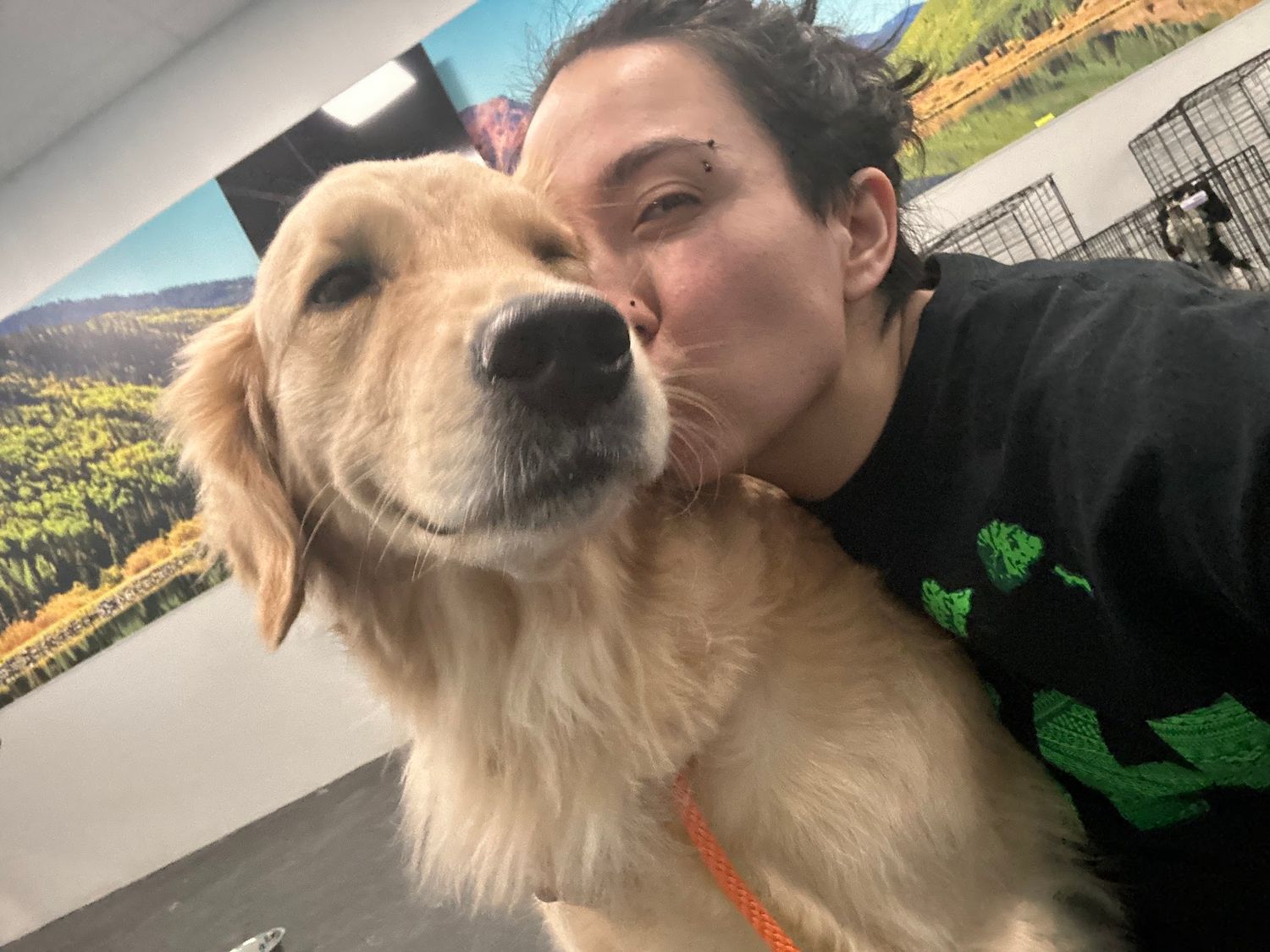 Woman in black hoodie kissing golden retriever dog on the cheek in a warm selfie.