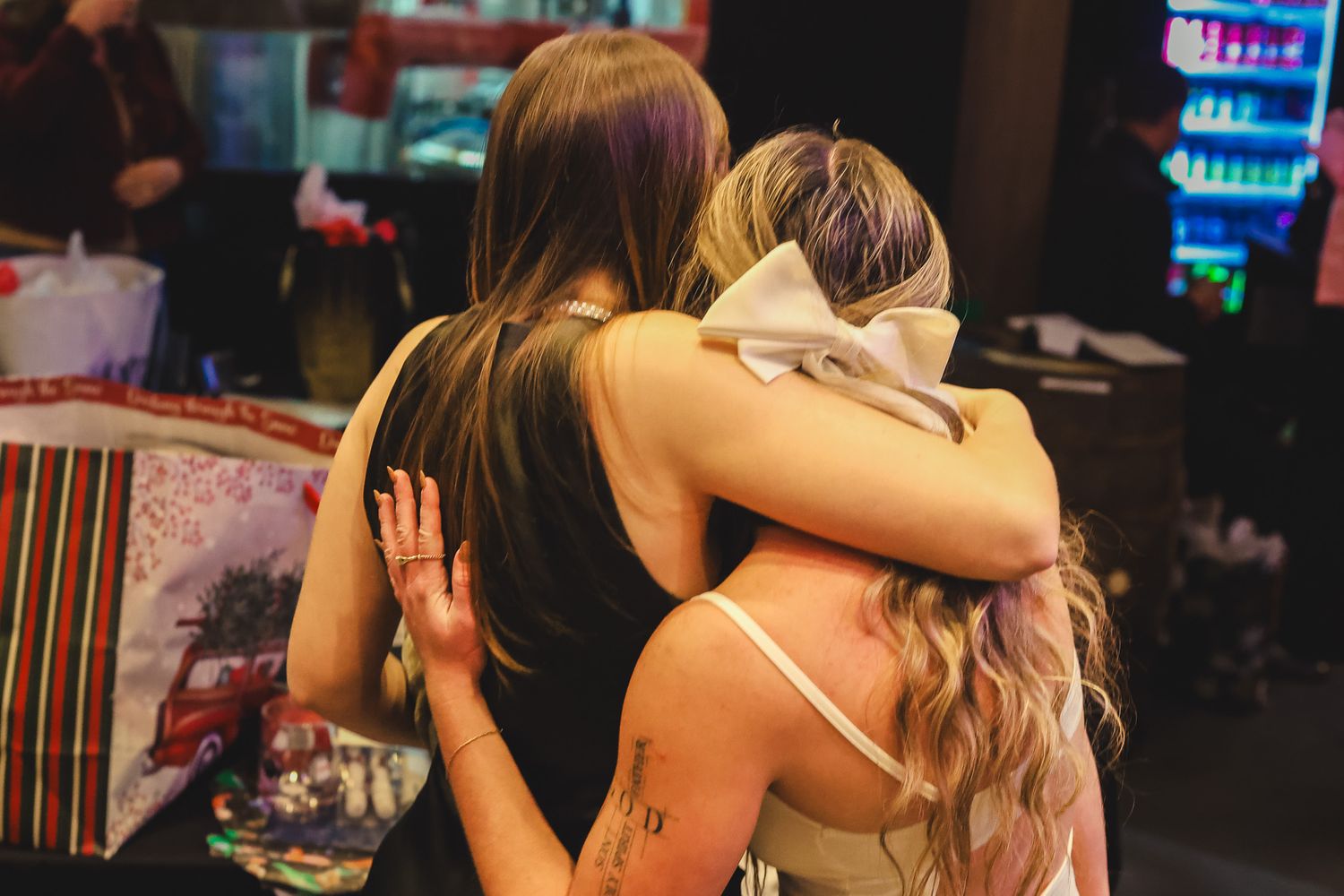 Two women sharing a warm hug at a casual indoor social gathering.