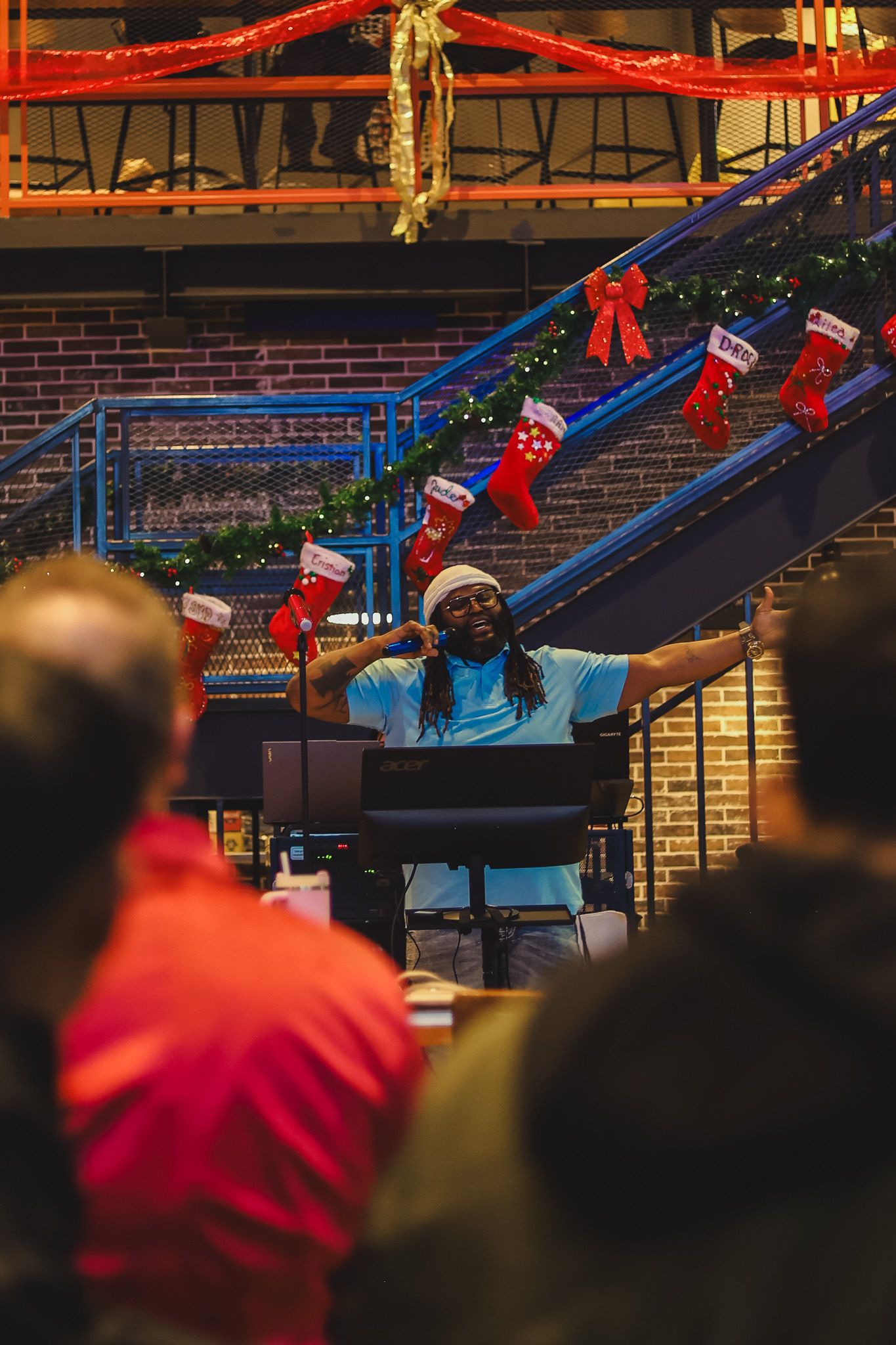 Musician performing at a festive Christmas event with holiday stockings and garland decorating a staircase in a brick venue.