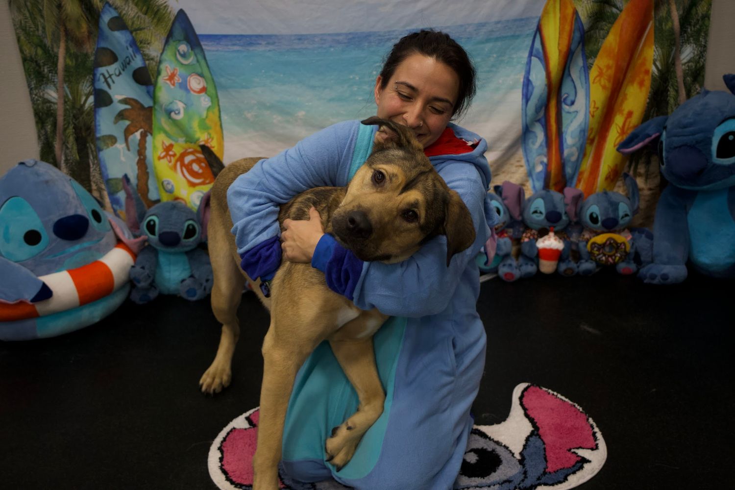 Smiling woman in blue hoodie holding a small tan puppy wrapped in a blue towel.