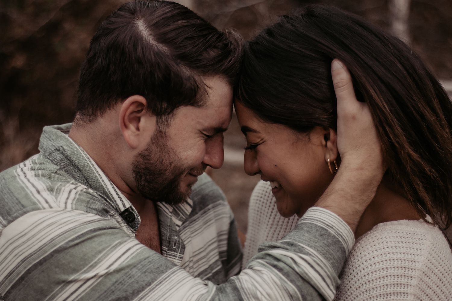 Romantic couple touching foreheads and smiling in an intimate outdoor engagement photo session.