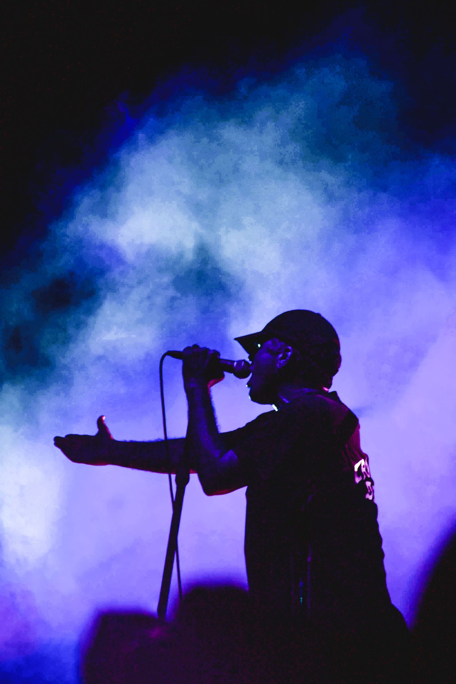 Silhouetted concert singer performing on stage surrounded by dramatic blue and purple smoke lighting.