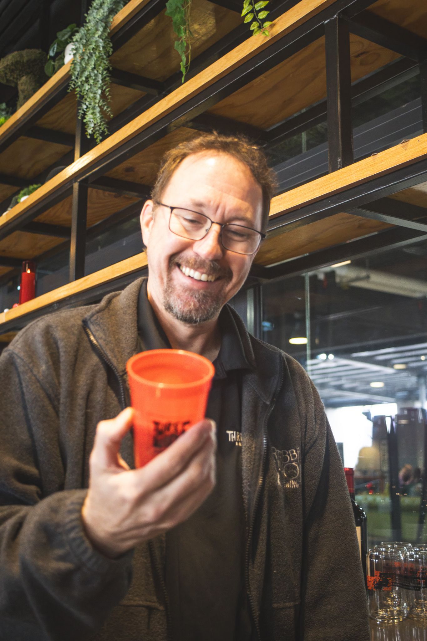 Smiling man with glasses holding an orange cup at a brewery bar.