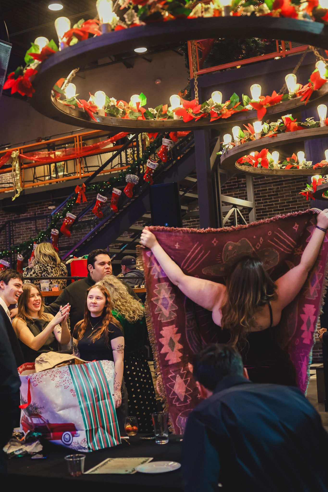 A woman holding up a colorful blanket at a Christmas party in a festively decorated venue.
