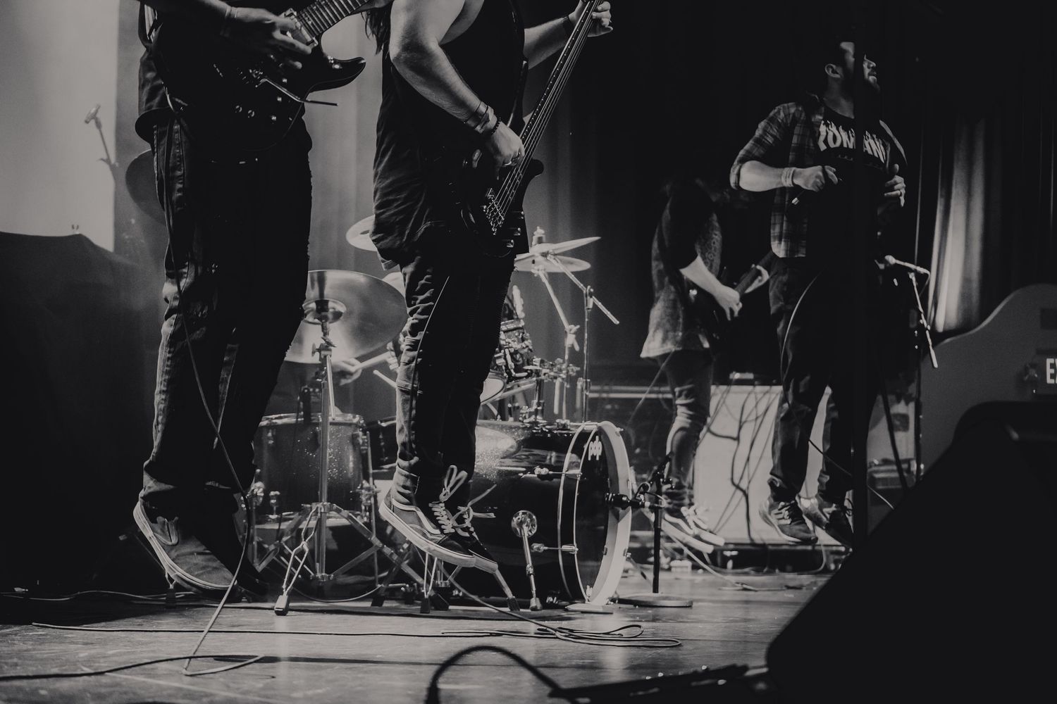 Black and white photo of a live band performing on stage with guitars and drums.