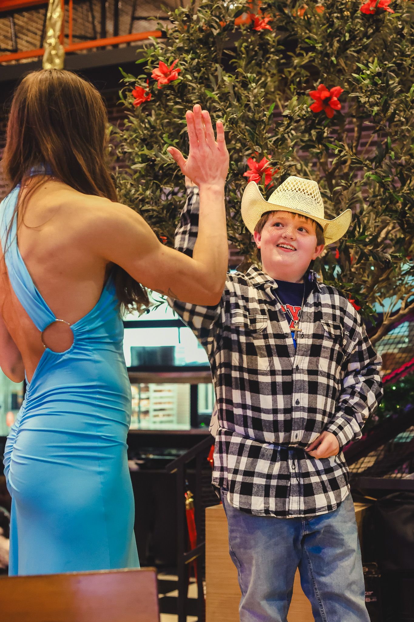 Young boy in cowboy hat and plaid shirt giving a high five to a woman in a blue dress.