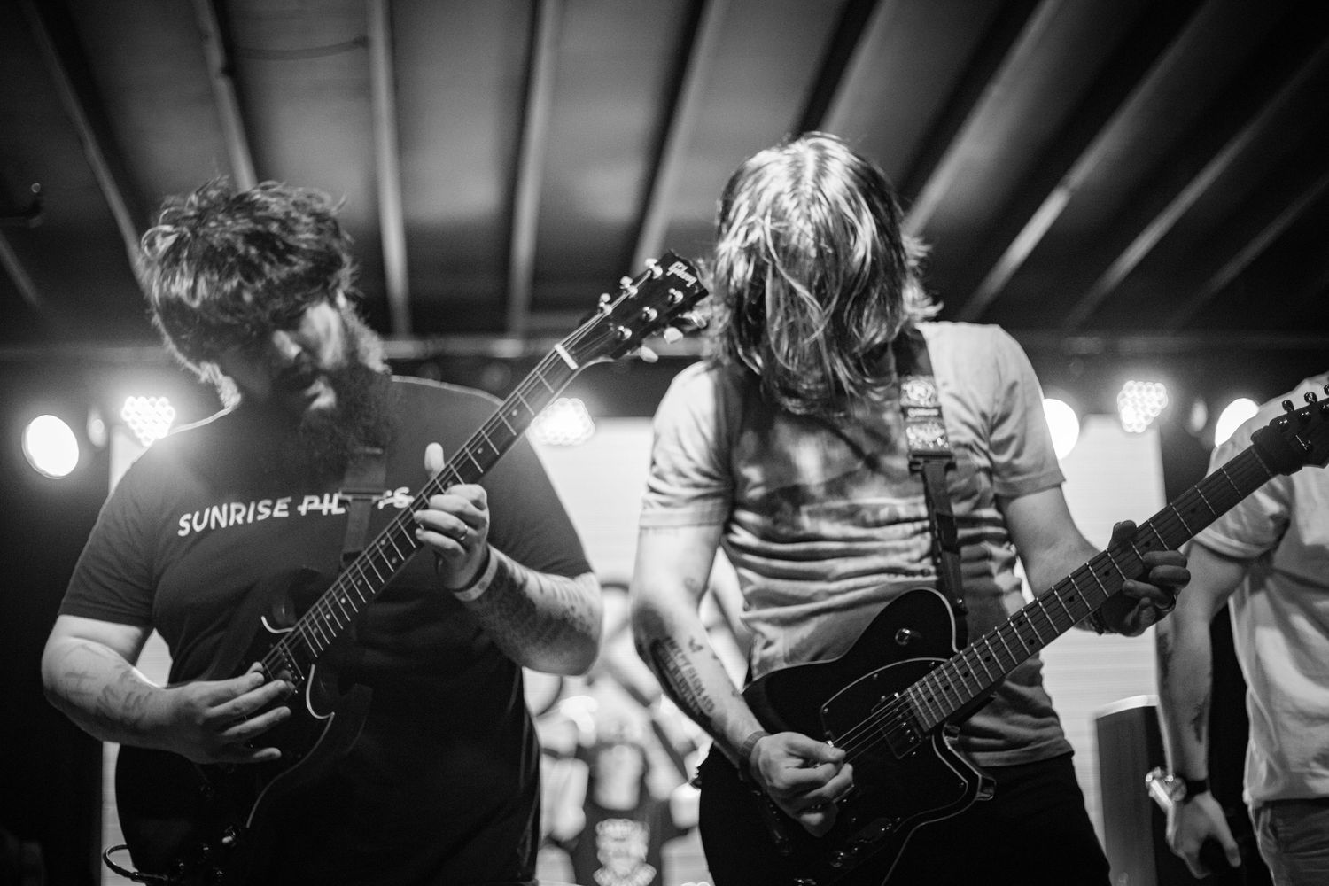 Black and white photo of two guitarists performing together on stage at a live music event.