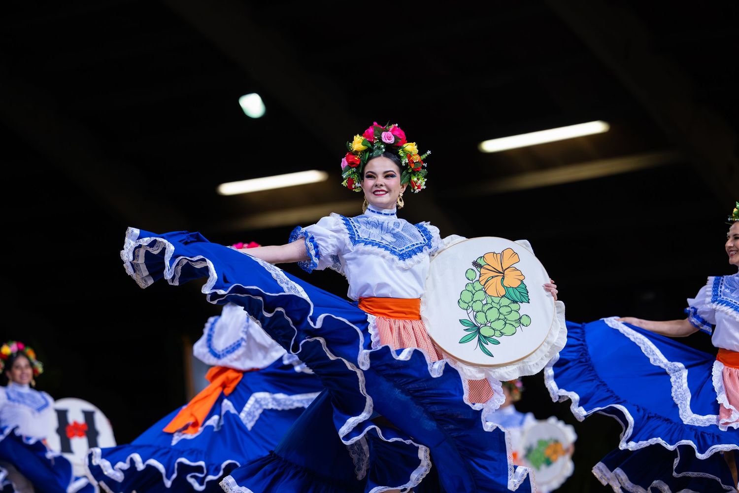 A colorful traditional Mexican folk dance performance featuring dancers in flowing blue and white dresses on stage.