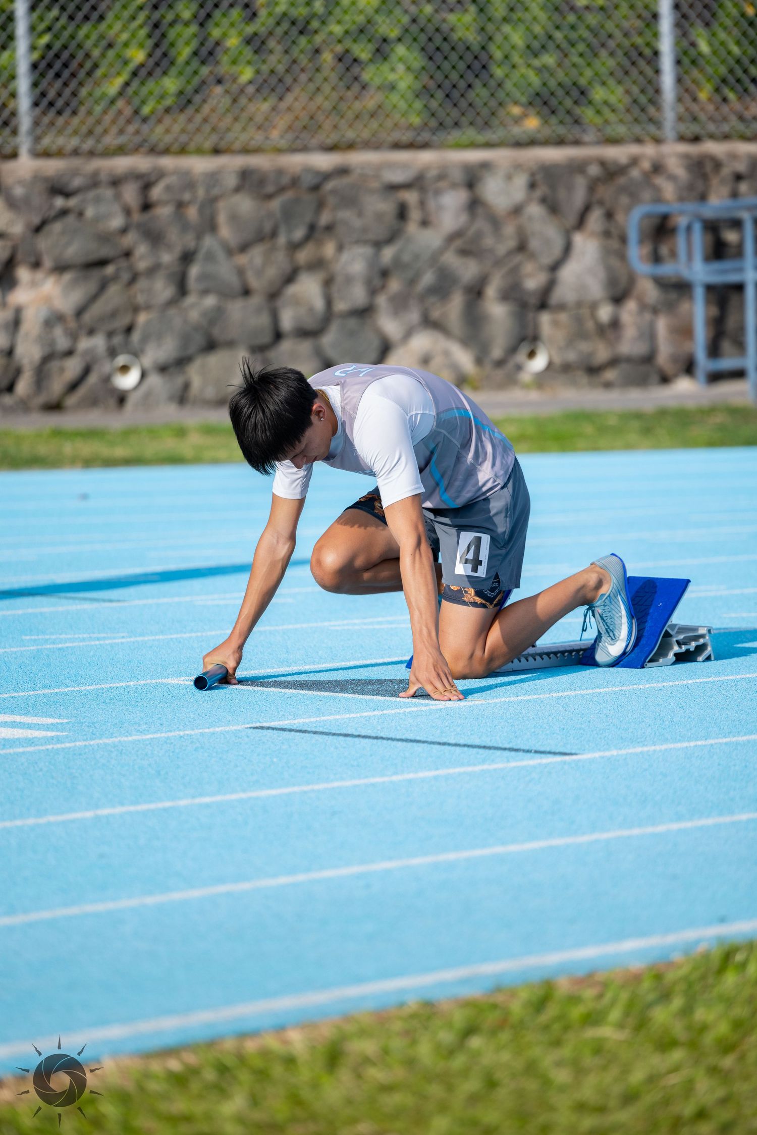 Athlete in starting position on blue running track preparing for sprint race at outdoor stadium.