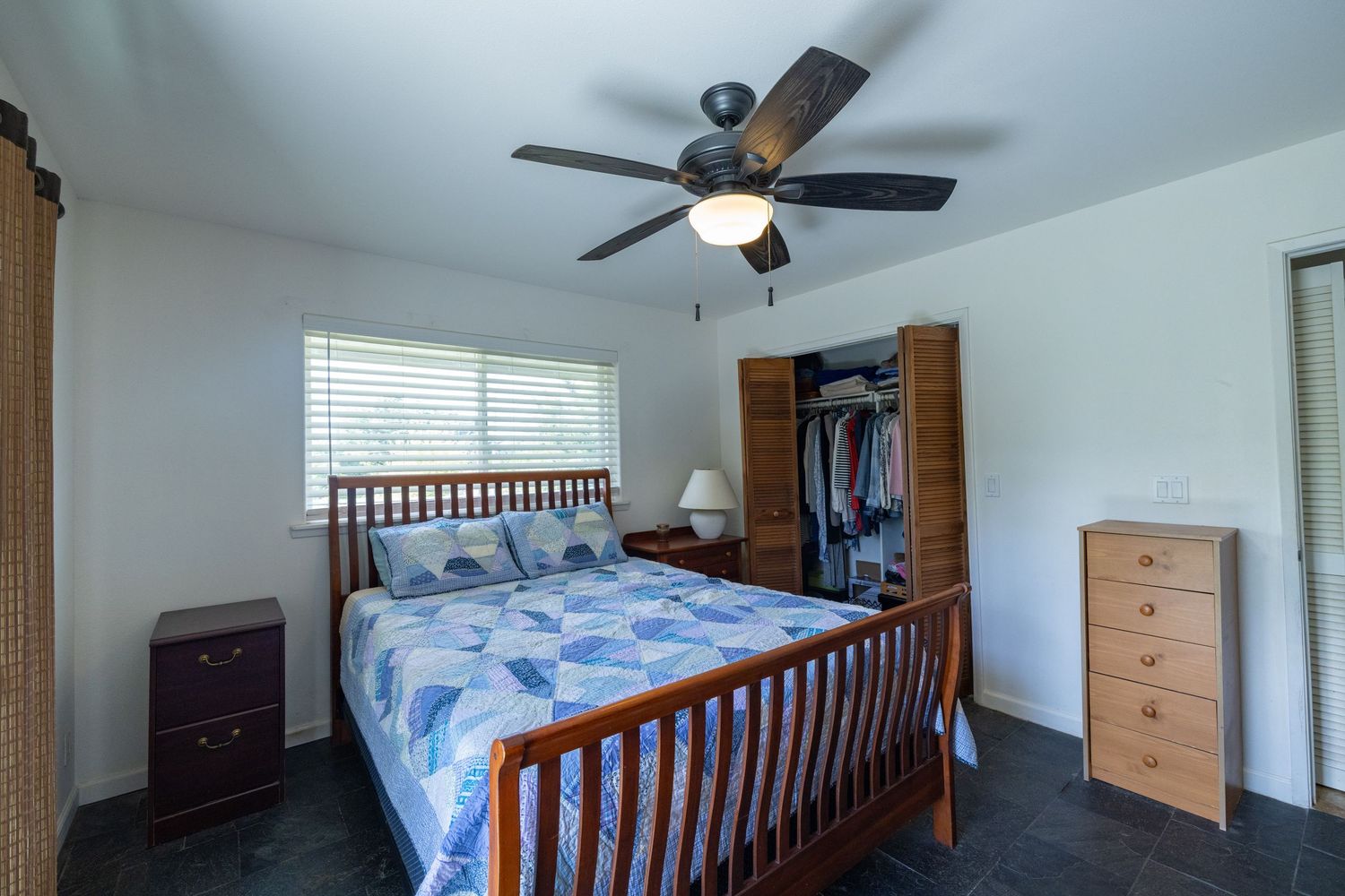 Spacious bedroom interior with wooden bed frame and ceiling fan.