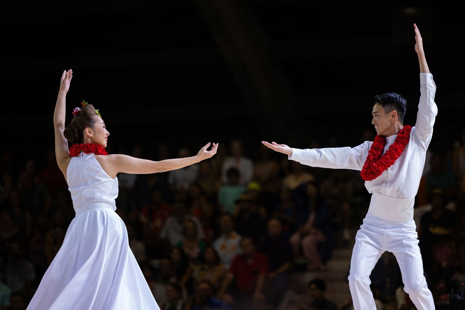 Two dancers in white costumes perform an expressive contemporary dance routine on a dark stage.