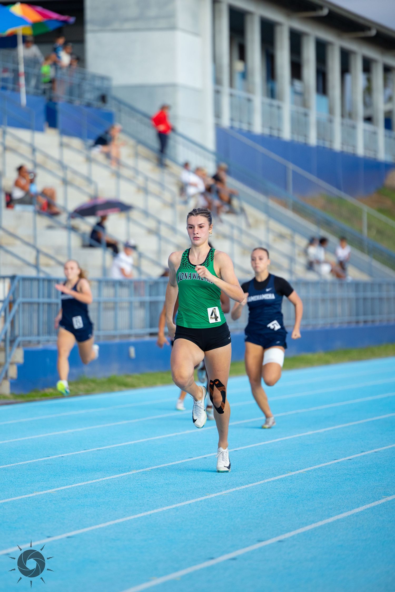 Runner in green singlet sprinting on a blue track during an outdoor competition.