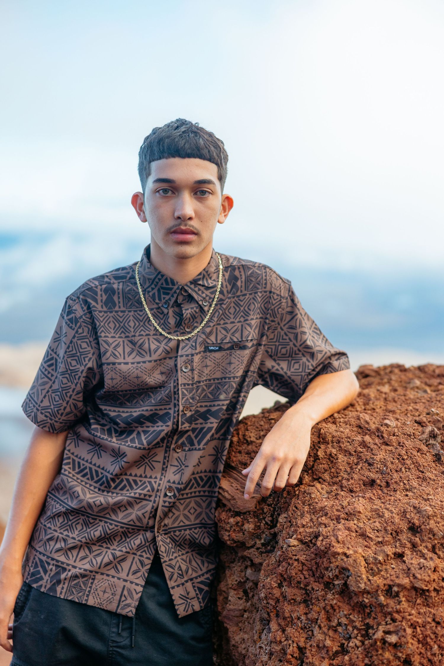 Portrait series against volcanic rocks wearing traditional Hawaiian print shirt in earth tones.