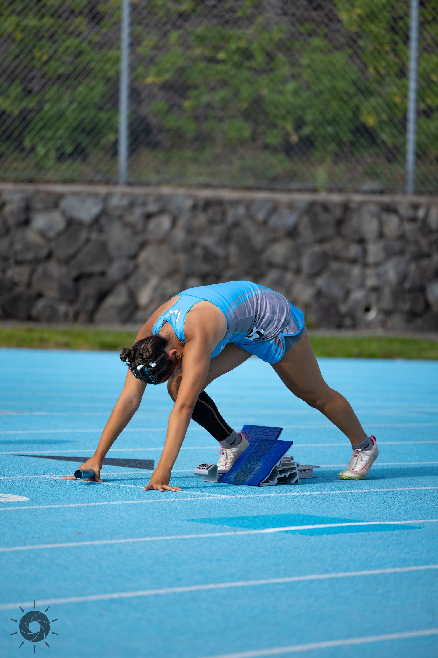 Sprinter in starting position on blue running track preparing for race start.
