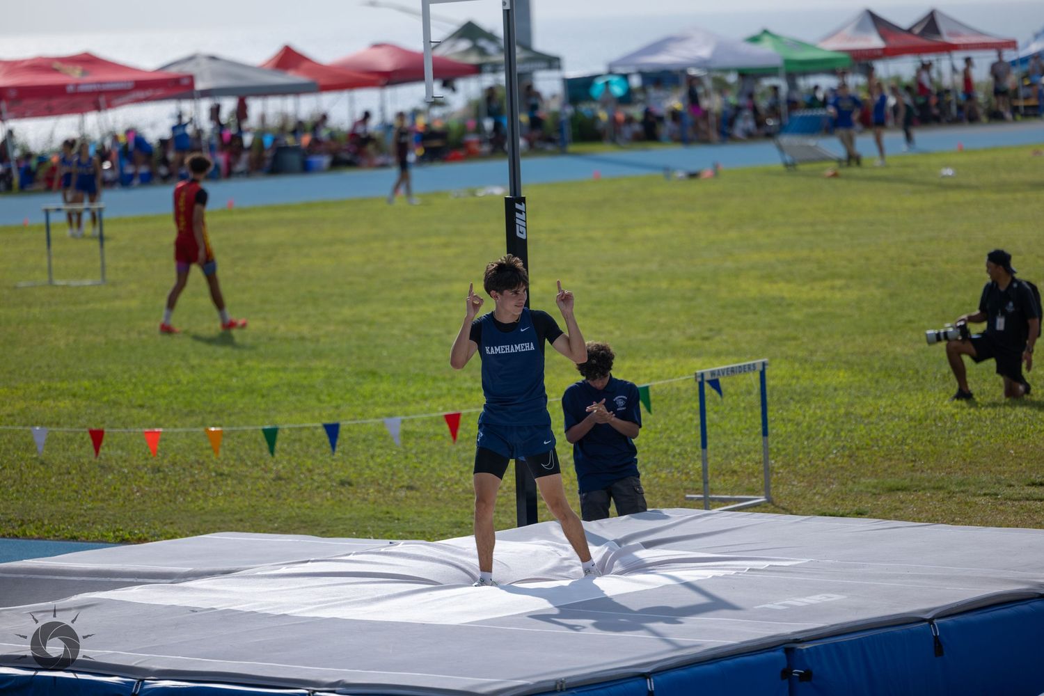 Athletes compete in a track and field event on a grassy field with colorful tents and spectators in the background.